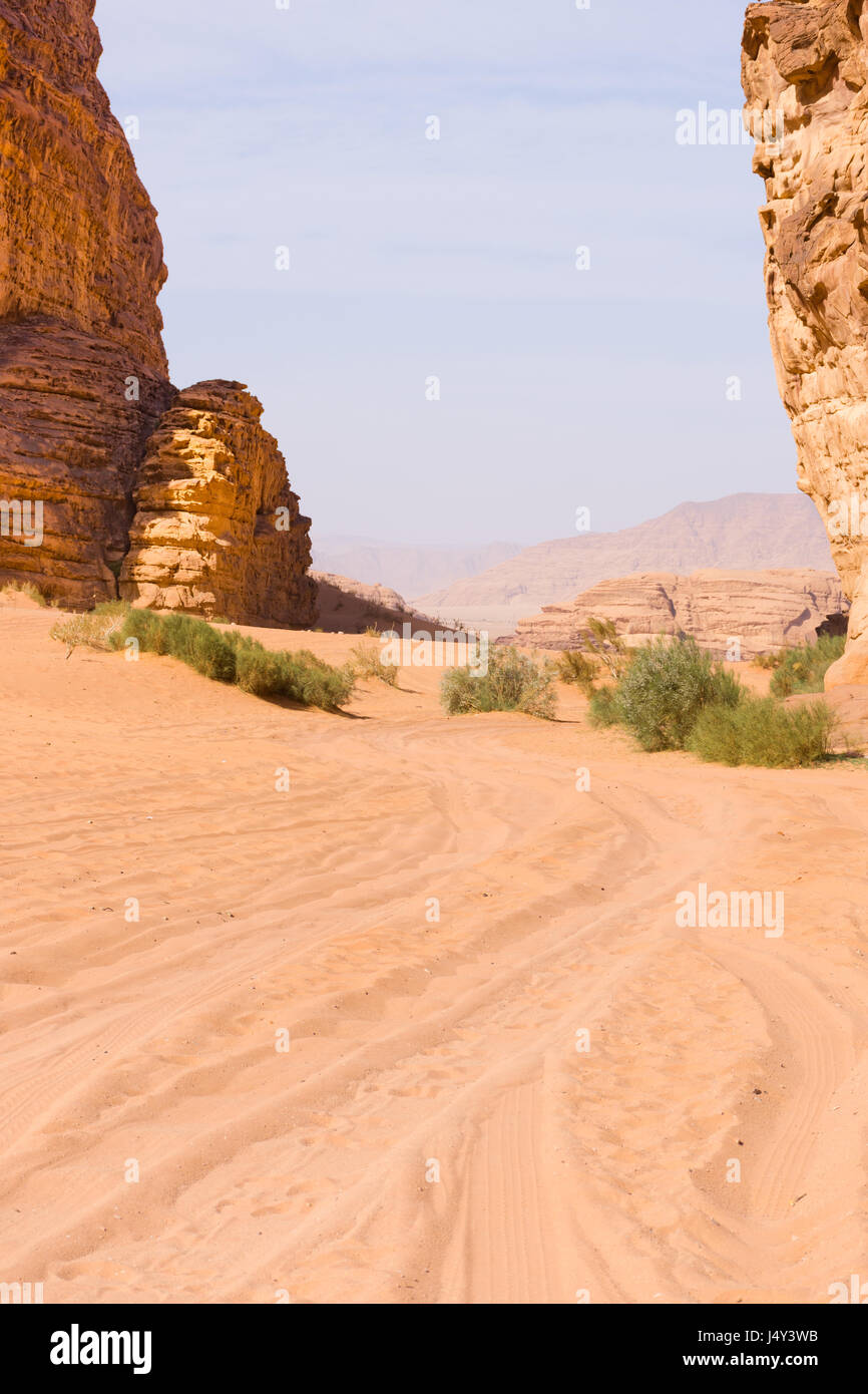 Pistas de las cuatro ruedas a través de Orange, Rose color arena del desierto de Wadi Rum en Jordania. Blue Sky está encima y escasa vegetación está presente. Foto de stock