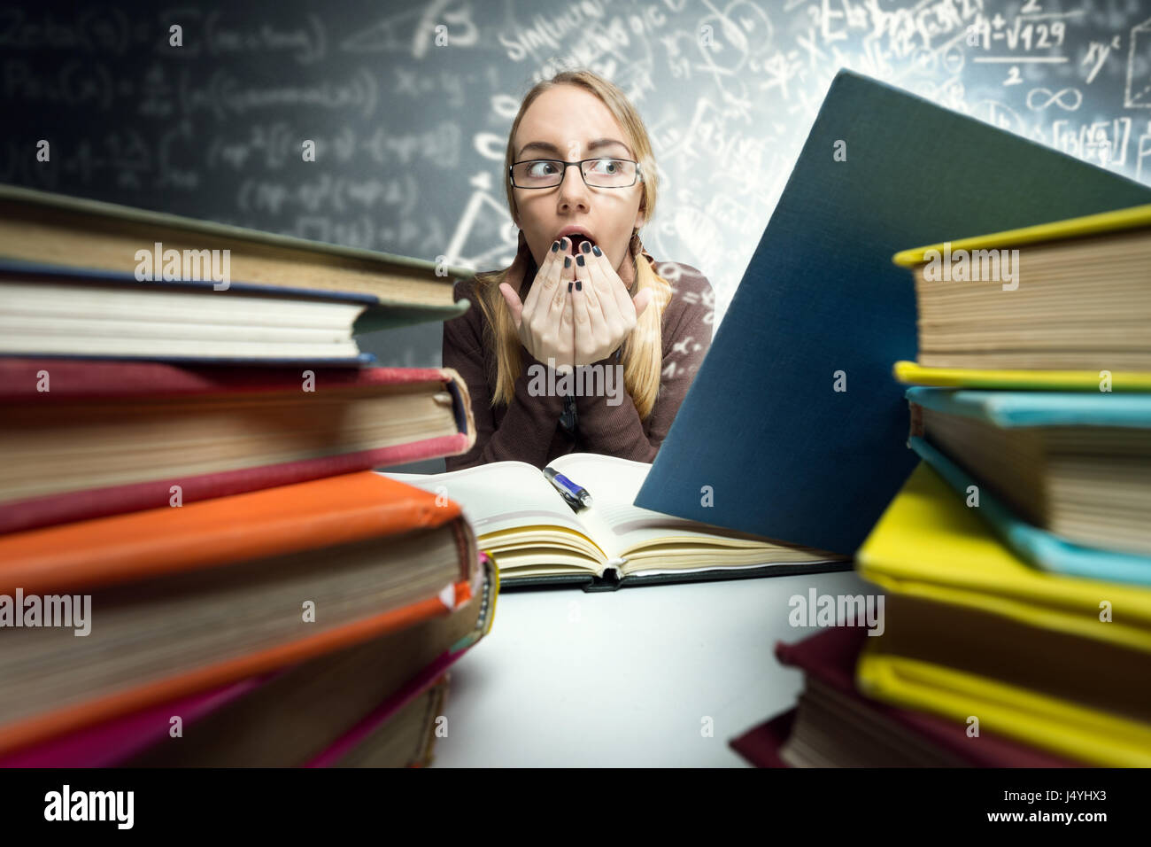 Conmocionado schoolgirl buscando en libro abierto con fórmulas mágicas Foto de stock