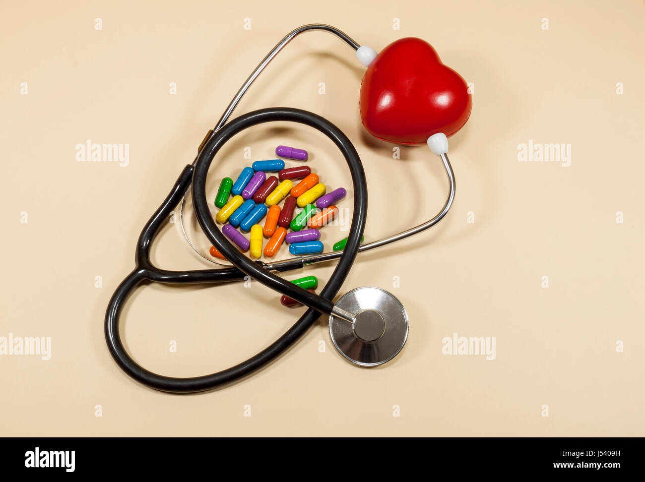 Rojo corazón esponjoso bloqueado entre los brazos de un estetoscopio médico y pastillas de colores , el concepto sobre la salud cardiovascular y el estilo de vida Foto de stock