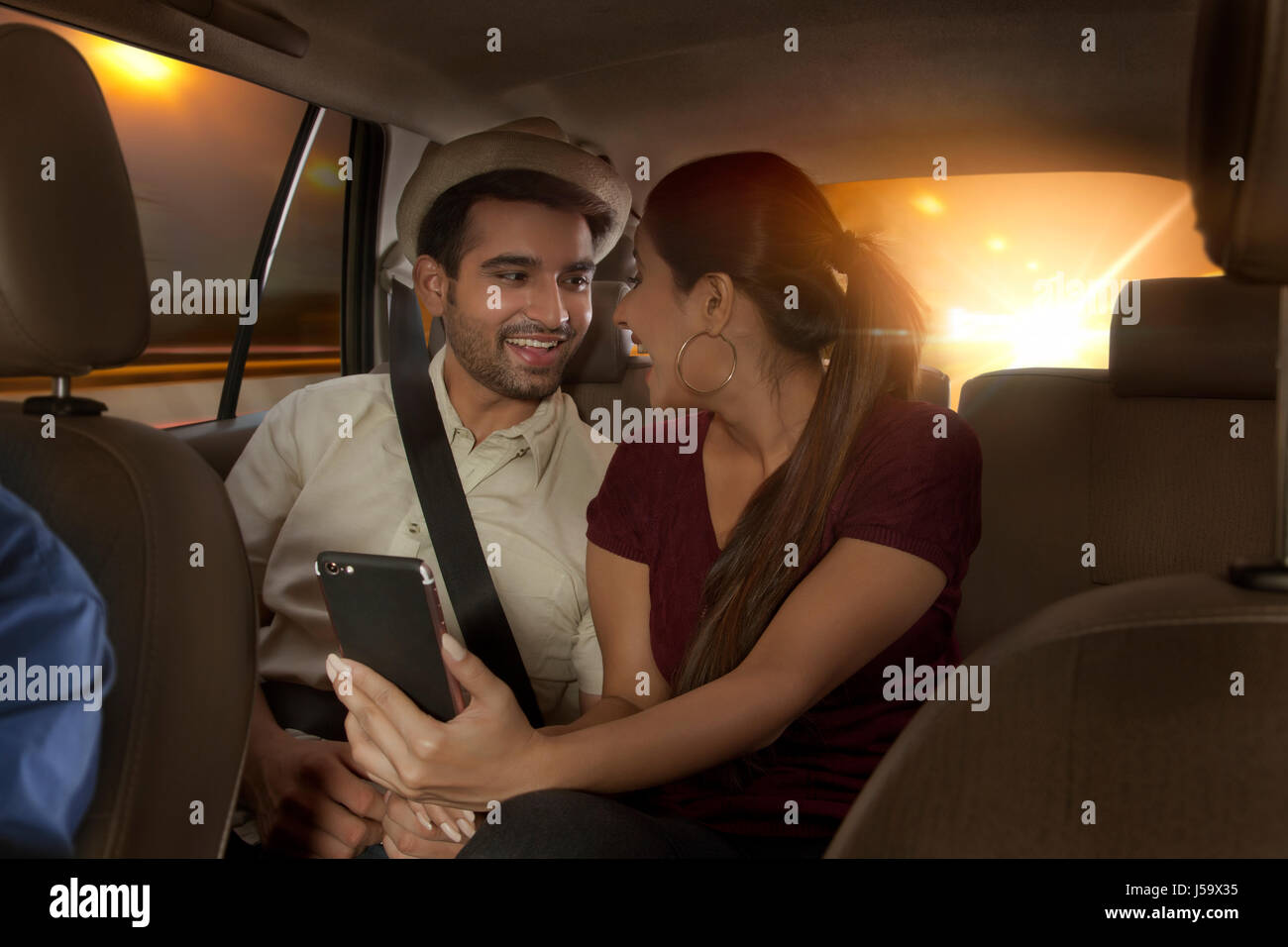 Sonriente joven pareja mirarse sentado en el asiento de atrás del coche Foto de stock