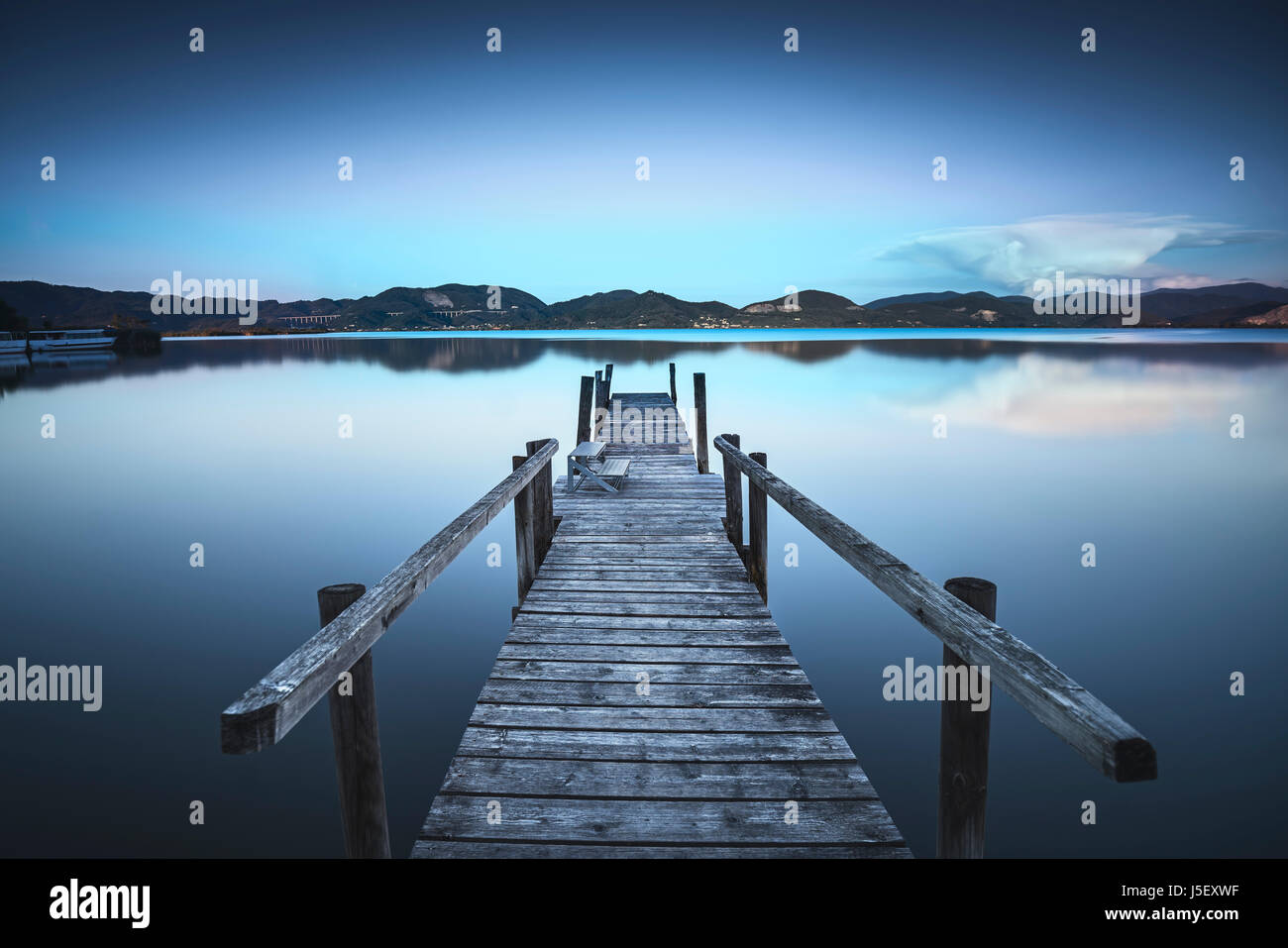 Muelle de madera o el embarcadero del lago azul cielo del atardecer y la reflexión del agua. La larga exposición, Versilia Massaciuccoli, Toscana, Italia. Foto de stock