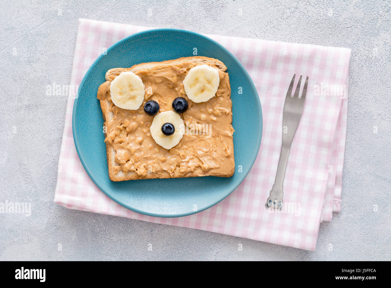 Teddy bear tostadas para niños. Mantequilla de cacahuete crujiente, banana  y arándanos tostadas con lindo oso de peluche cara en una placa azul sobre  rosa accidentada textil. A Fotografía de stock -