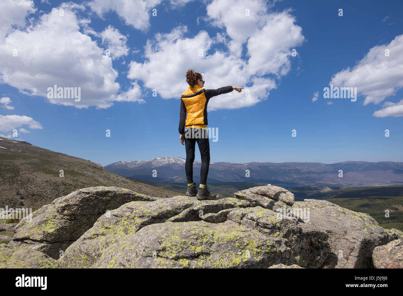 Deporte senderismo o trekking mujer con ropa de color amarillo y negro, de  pie sobre la roca, pico hacia arriba con la mano horizon en la distancia,  un valle de Lozoya Fotografía