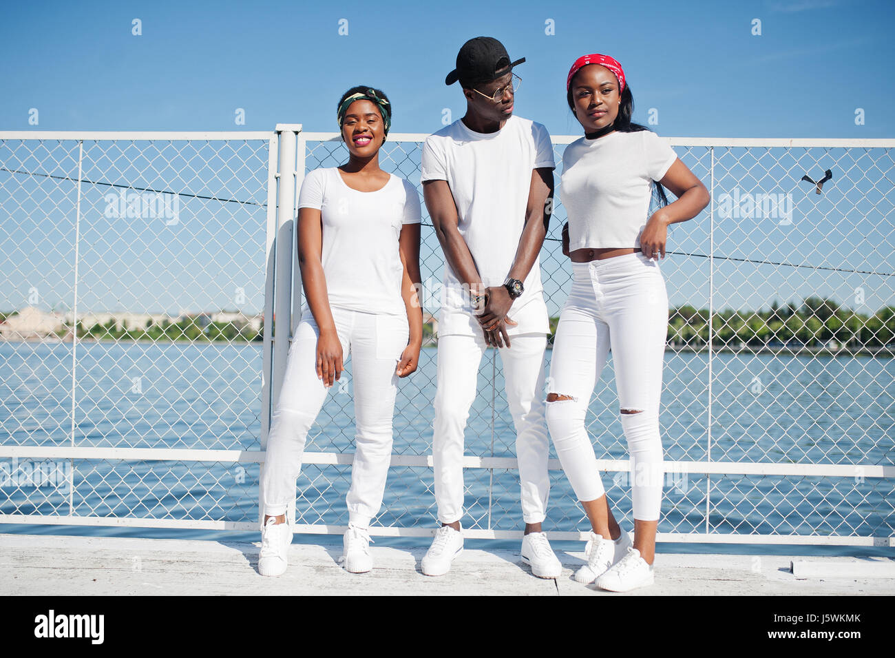 Tres elegantes amigos afroamericanos, el desgaste de la ropa blanca en el muelle en playa contra la jaula. La moda de calle de los jóvenes negros. Hombre Negro dos Fotografía