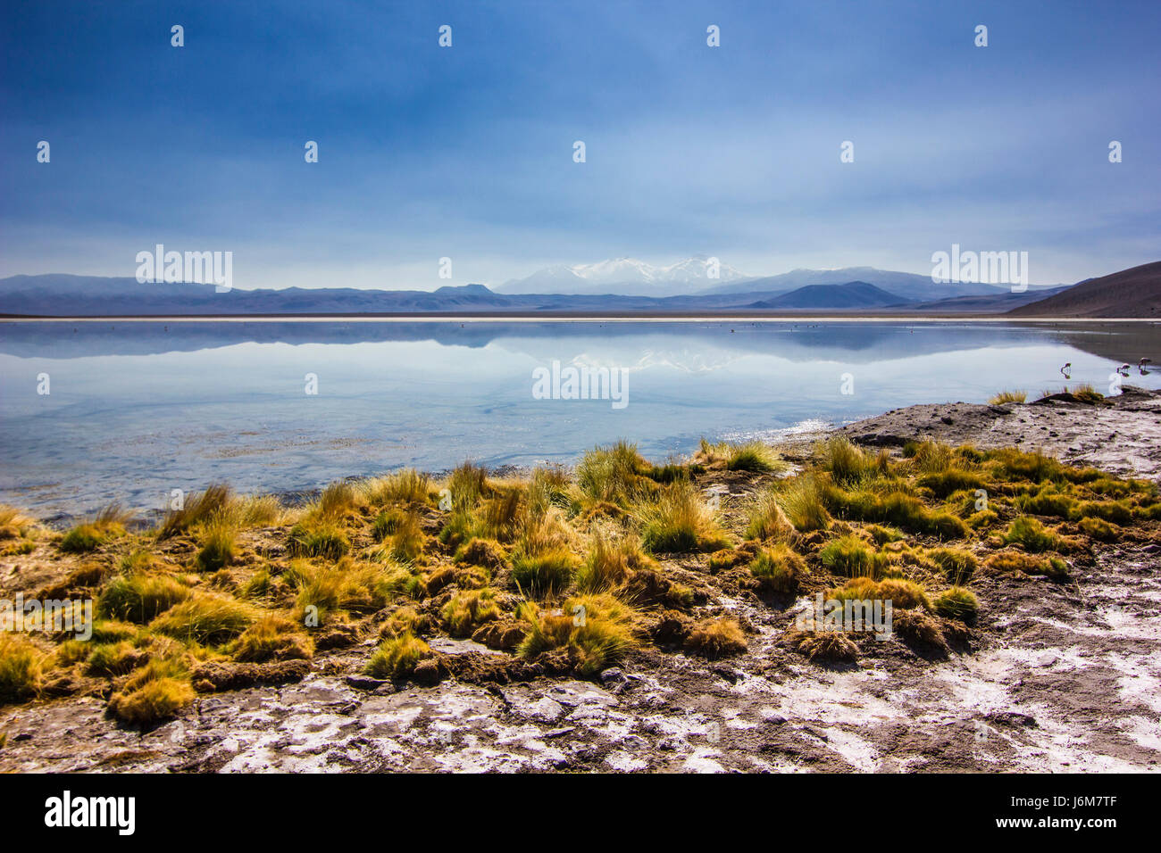 La superficie del espejo del lago de montaña, rodeado de altas cumbres y hierba amarilla Foto de stock