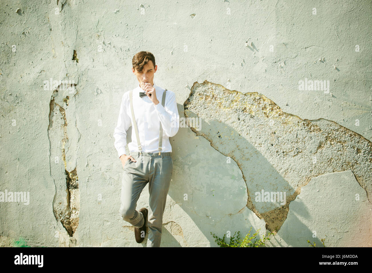 Joven hombre flaco, elegantemente elegantemente vestido con camisa blanca, pantalón  gris con tirantes y pajarita. Fuma un cigarrillo electrónico en fondo  Fotografía de stock - Alamy