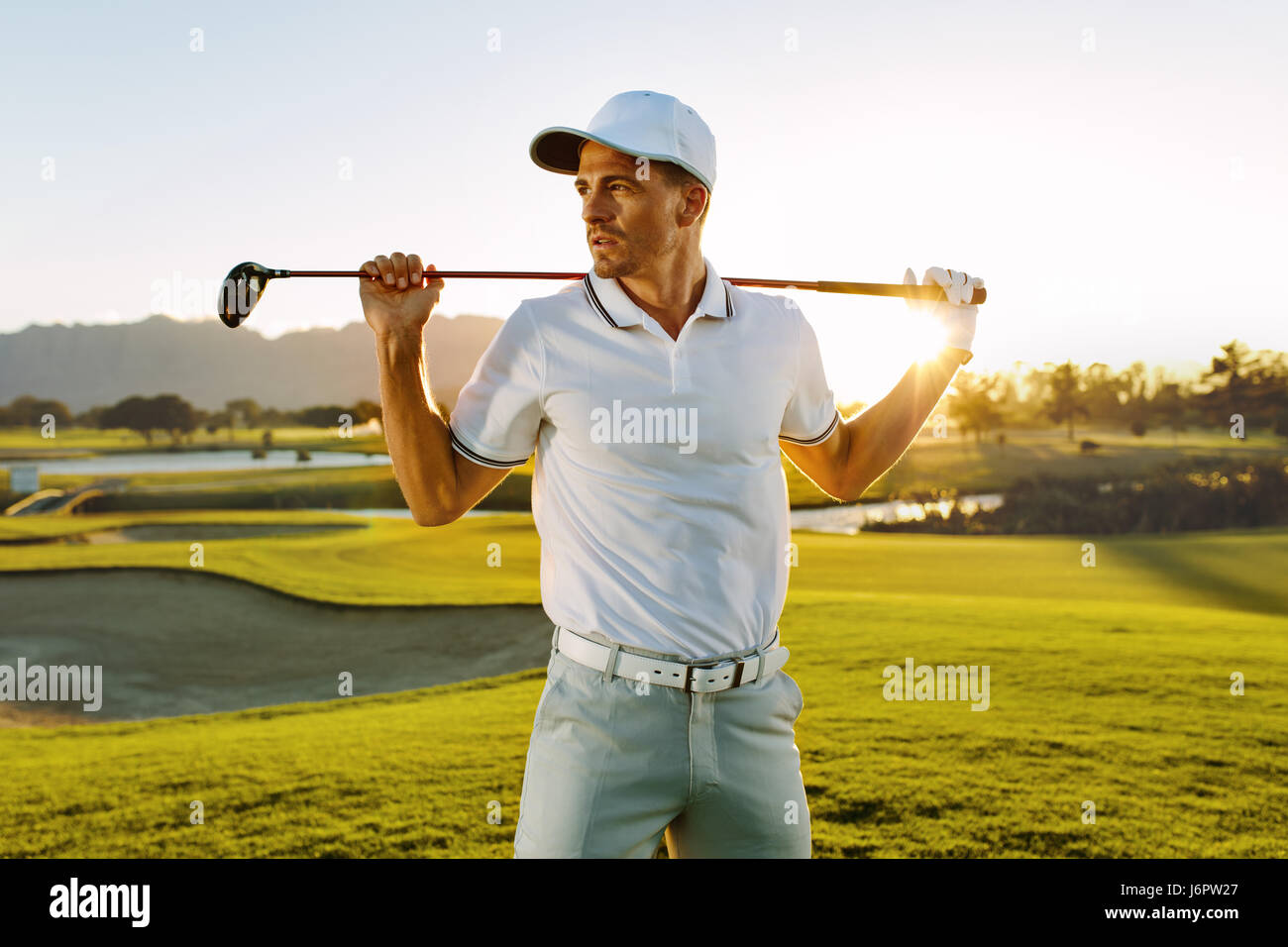 Foto de golfista masculino con club de golf en curso. Joven sosteniendo un club de golf y apartar la mirada en un día soleado. Foto de stock