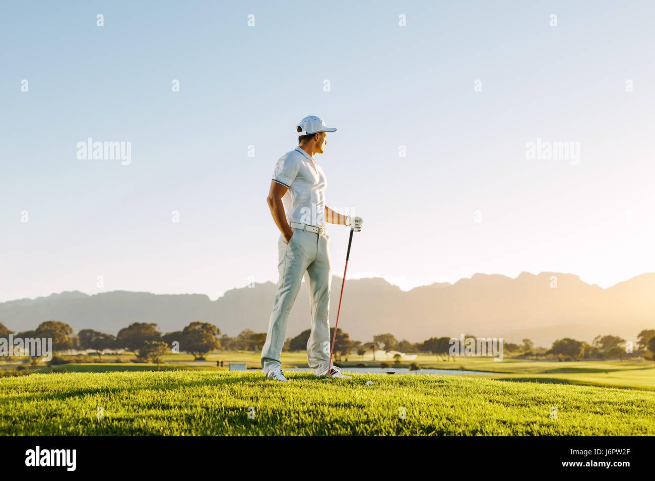 Longitud total de jóvenes caucásicos hombre permanente en campo de golf en un día de verano. Golfista masculino la celebración de golf club de campo. Foto de stock