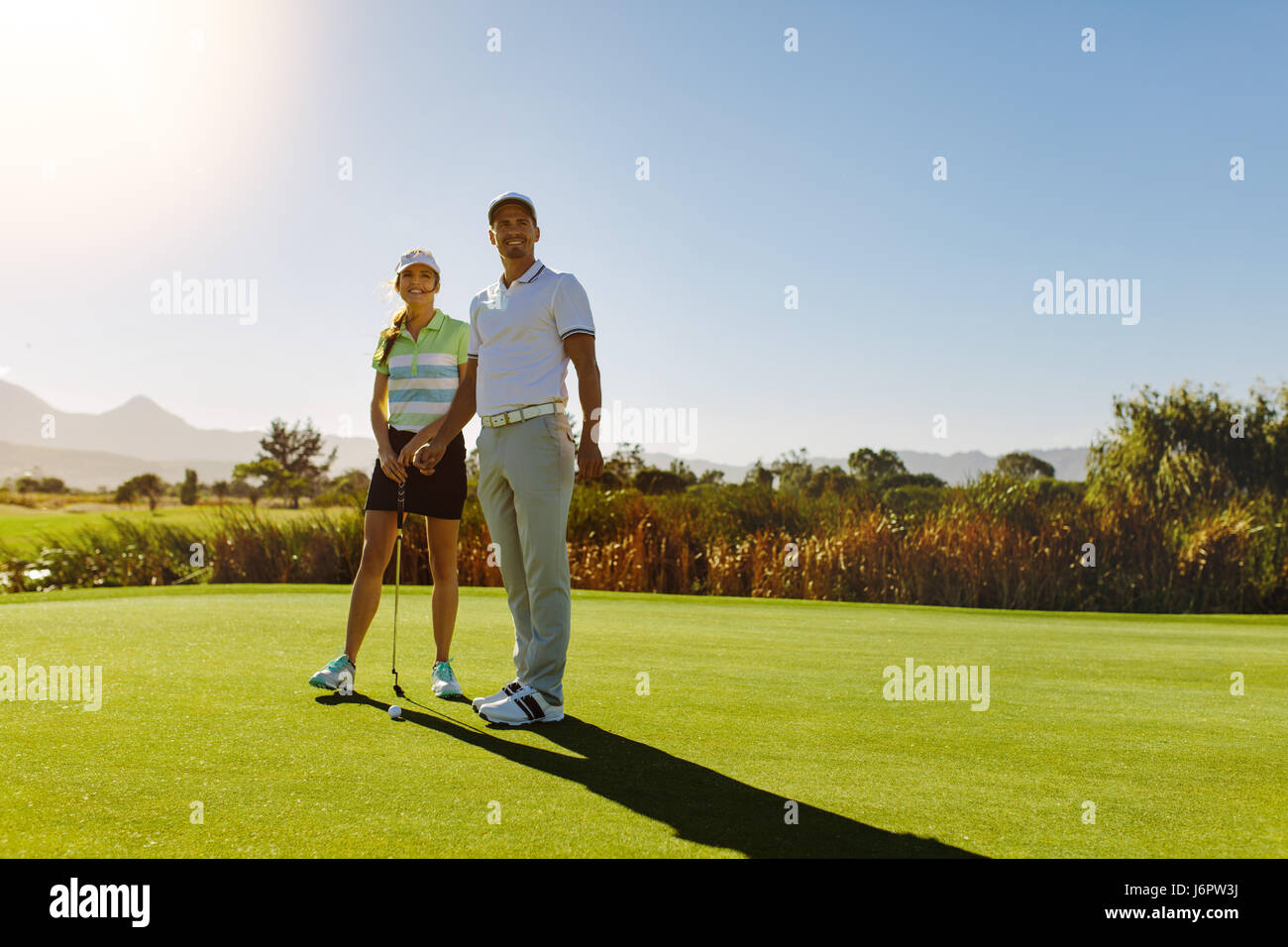 Pareja joven en el putting green de golf. Los golfistas masculinos y femeninos en el campo en día soleado. Foto de stock