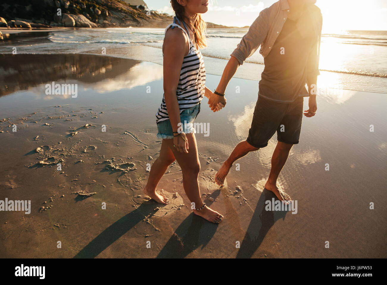Disparó al aire libre de amorosa pareja joven caminando por la orilla del mar cogidos de la mano. El hombre y la mujer joven en la playa caminando juntos. Foto de stock