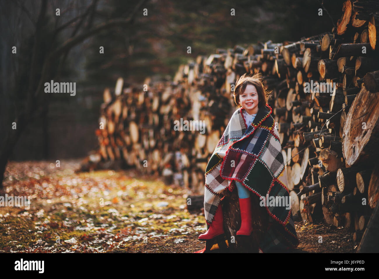 Chica sentada por log pile envuelto en Manta Foto de stock