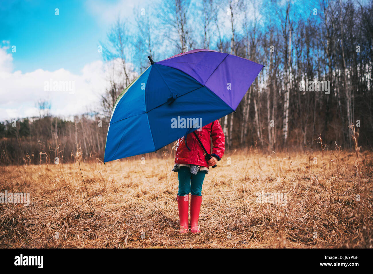 Niña de pie en el paisaje rural con un paraguas multicolor Foto de stock