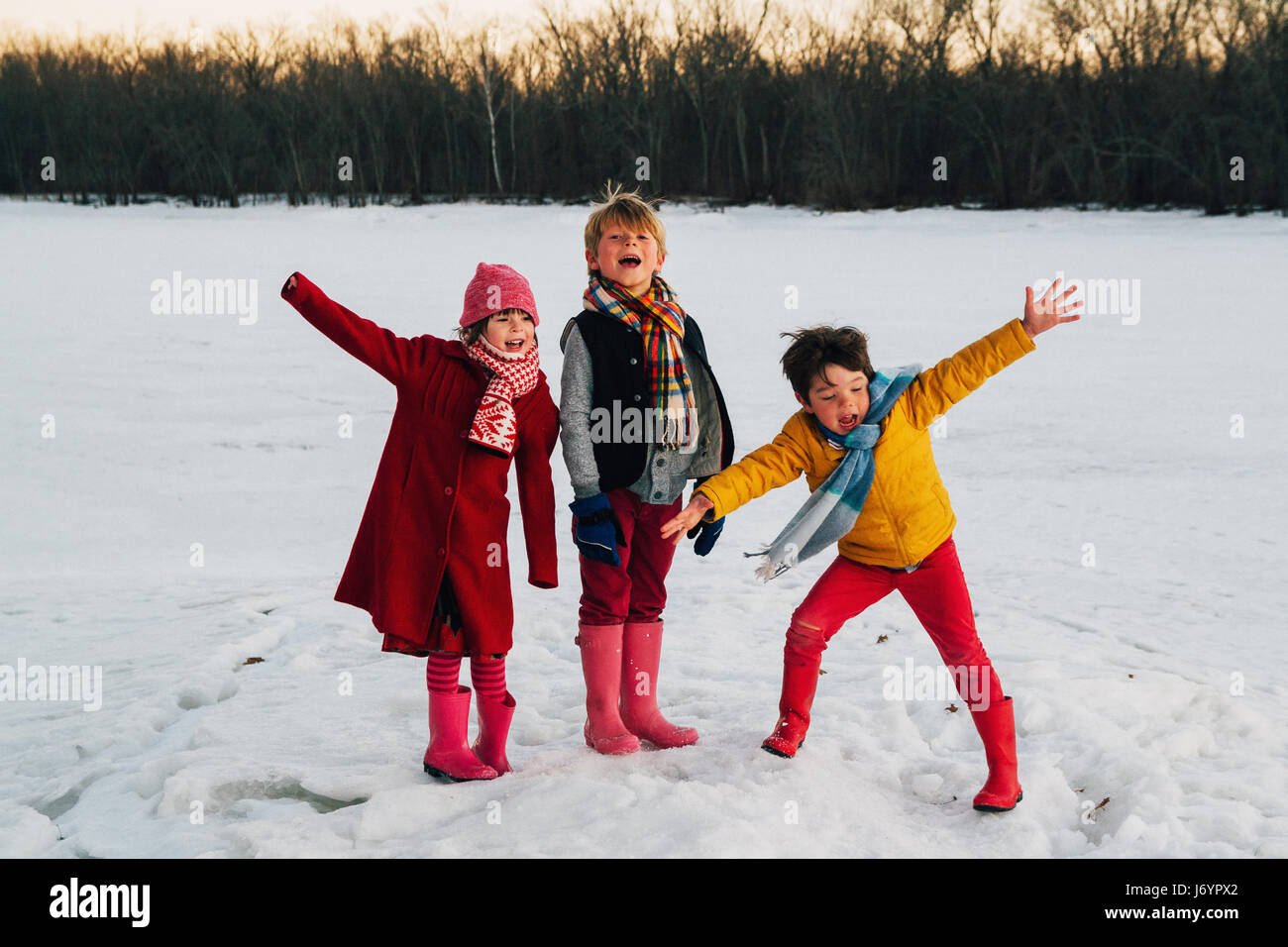 Tres niños de pie en la nieve con los brazos extendidos gritando Foto de stock