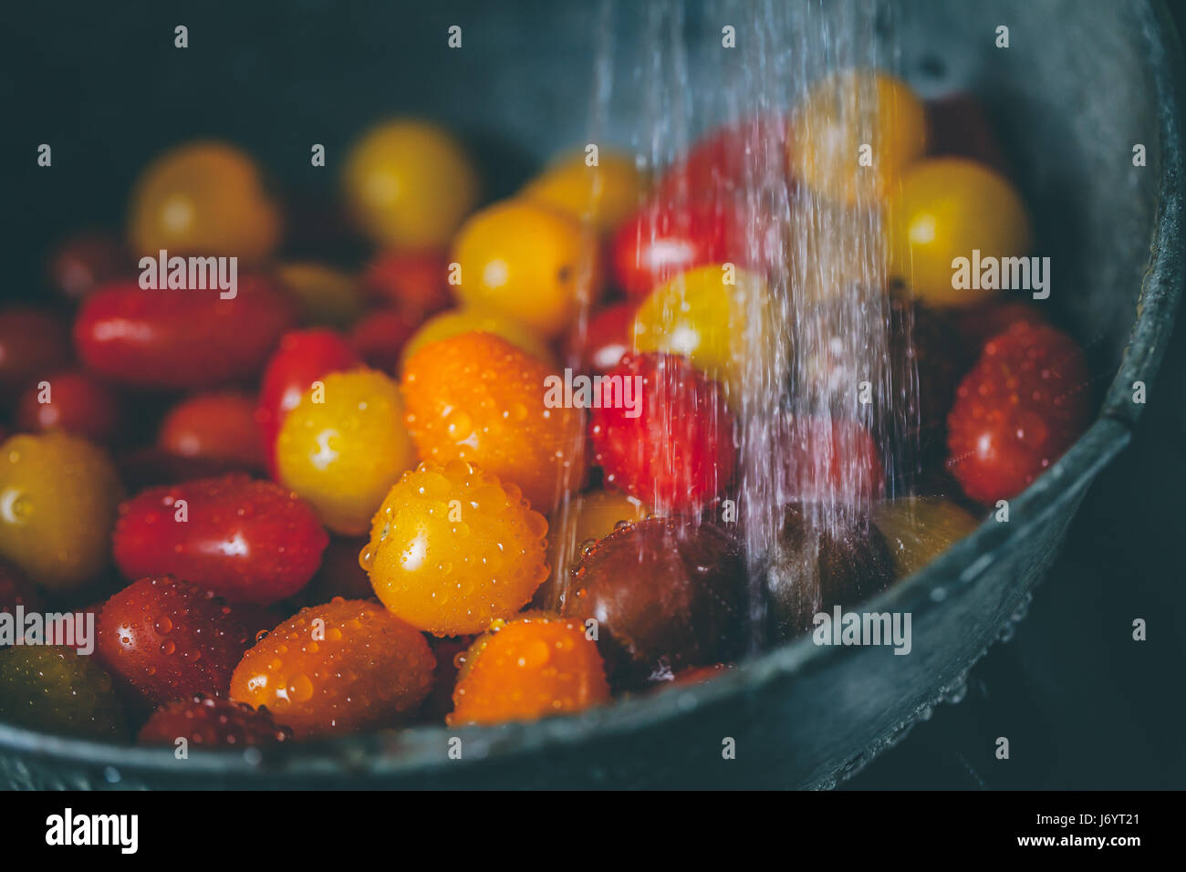 Tomates Cherry en un colador bajo el grifo de agua Foto de stock