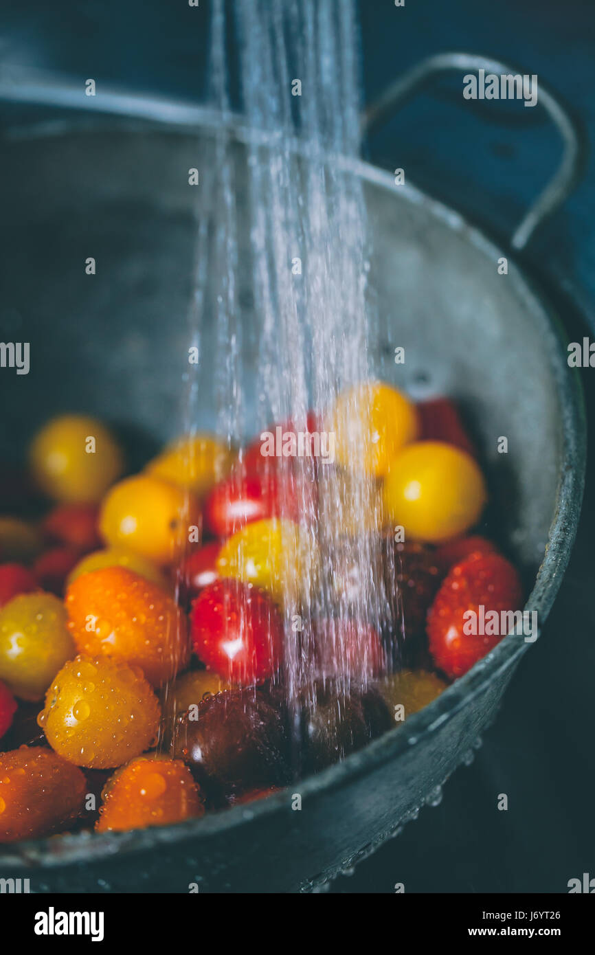 Tomates Cherry en un colador bajo el grifo de agua Foto de stock