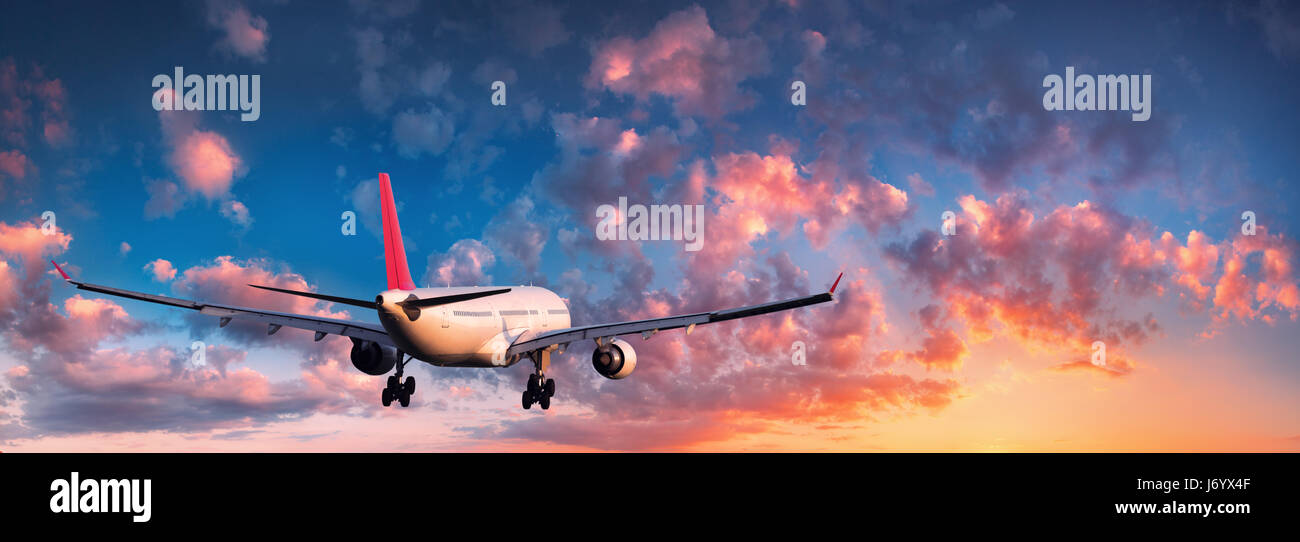 En avión. Paisaje con big white avión está volando en el cielo azul con nubes rojas y anaranjadas en colorido atardecer. Los viajes. Pasajero airli Foto de stock