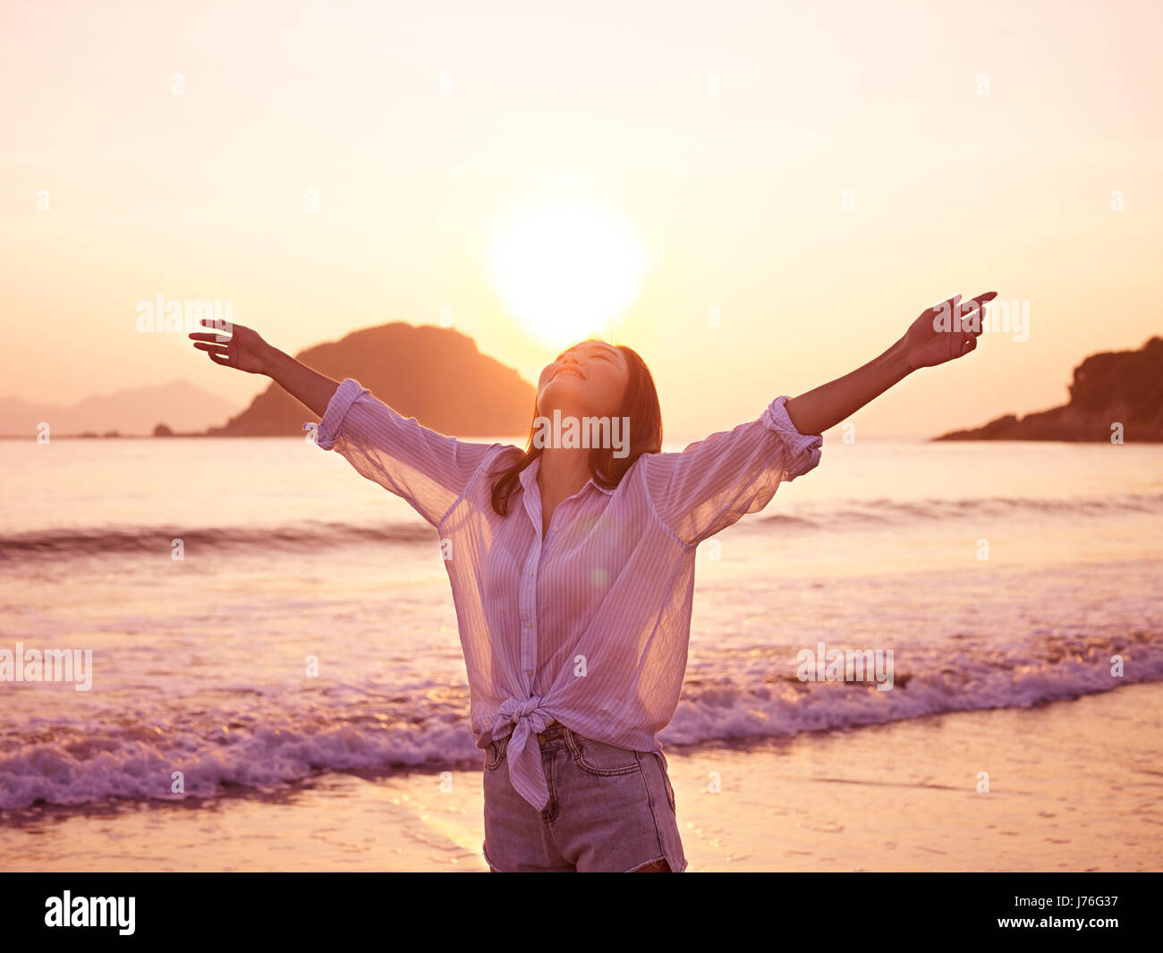 Joven mujer asiática disfrutando del sol por la mañana temprano con los brazos abiertos en la playa. Foto de stock