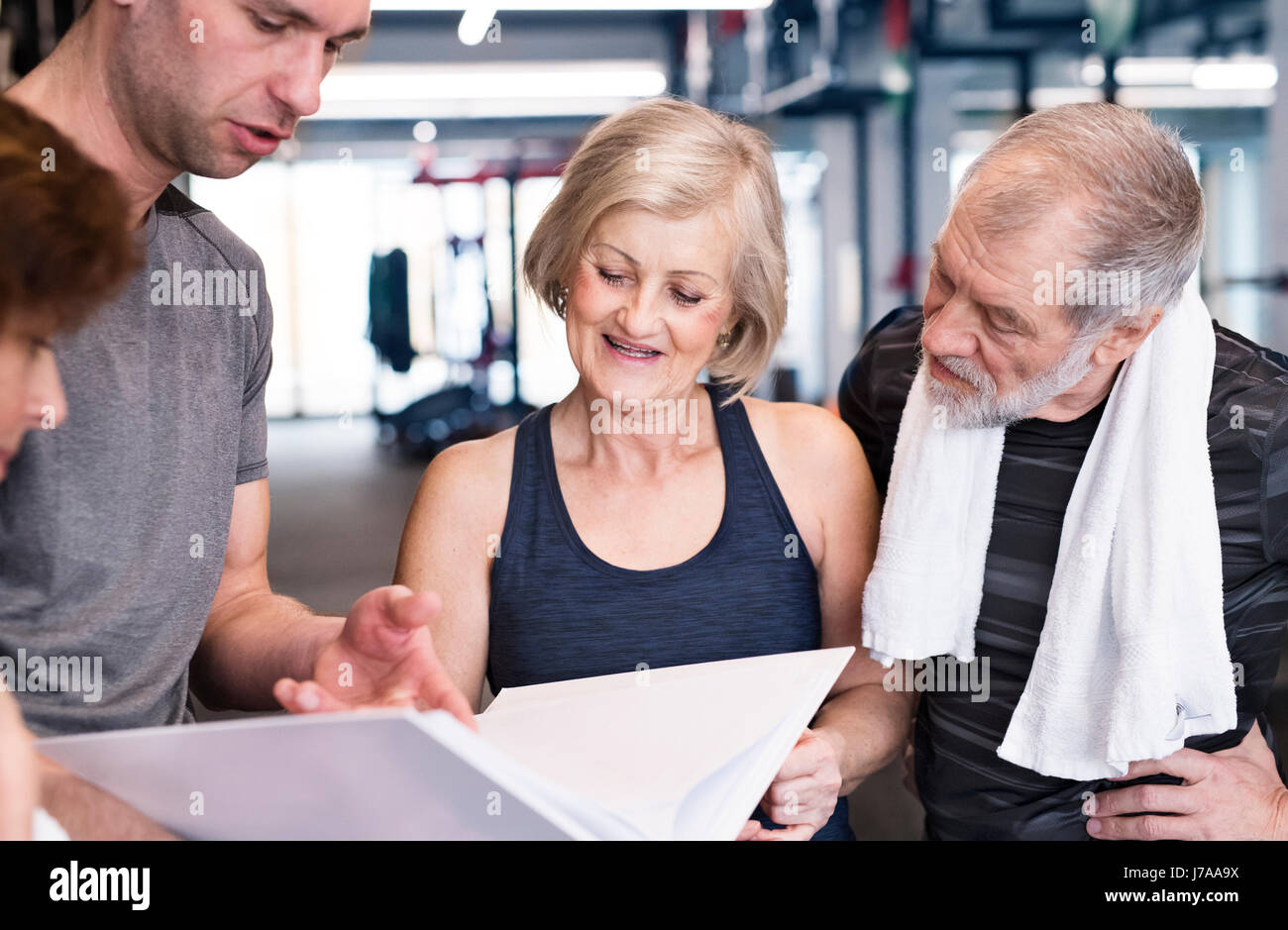 Grupo de colocar mayores y un entrenador personal en un gimnasio busca en la carpeta Foto de stock