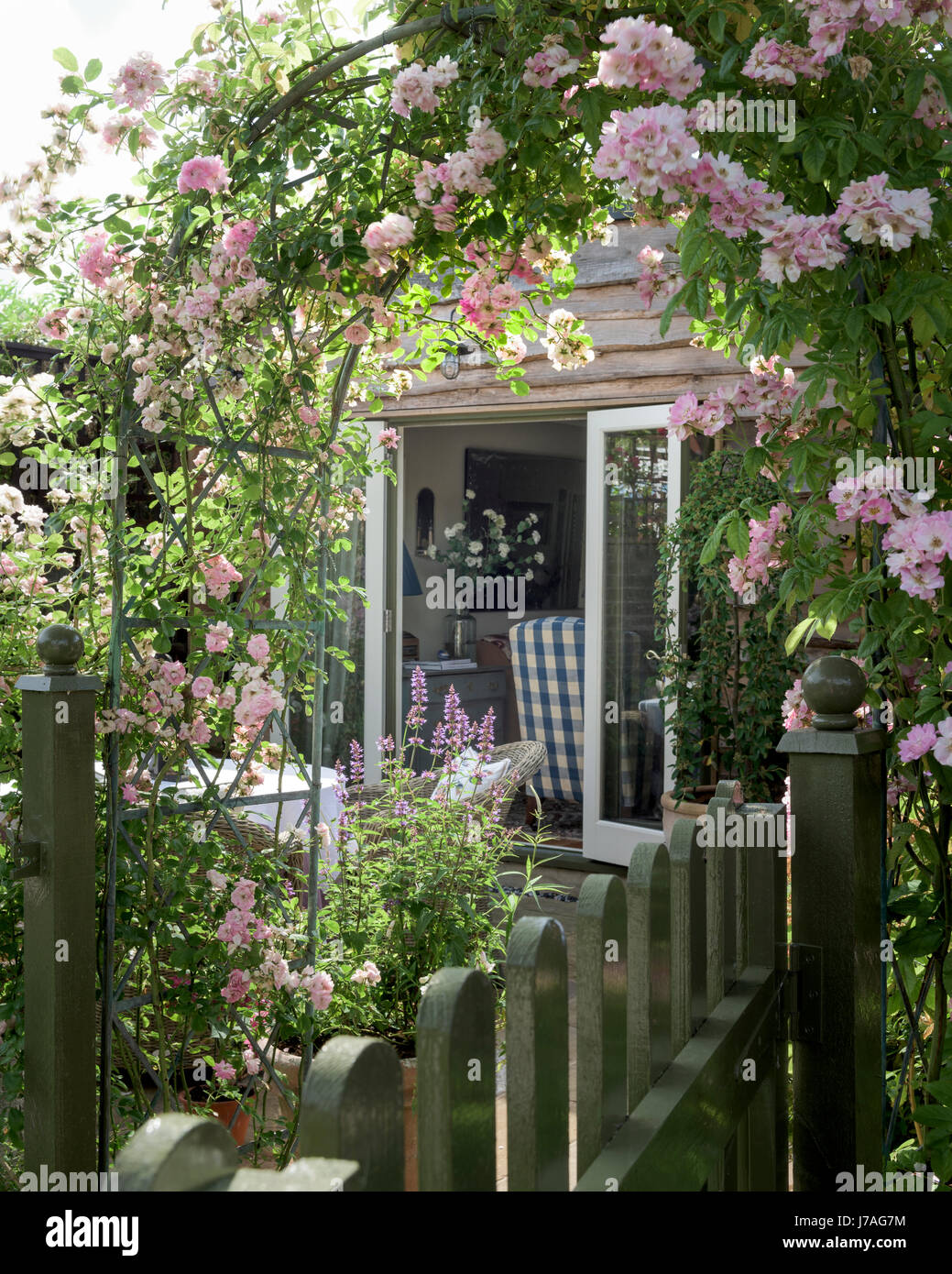 Vista a través de la rosa de jardín arco revestido de roble a casa con ventanas francesas de extensión Foto de stock