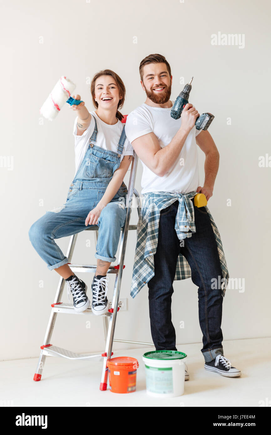 Feliz pareja joven mostrando herramientas para reparar mientras está de pie  cerca de la escalera aislada Fotografía de stock - Alamy