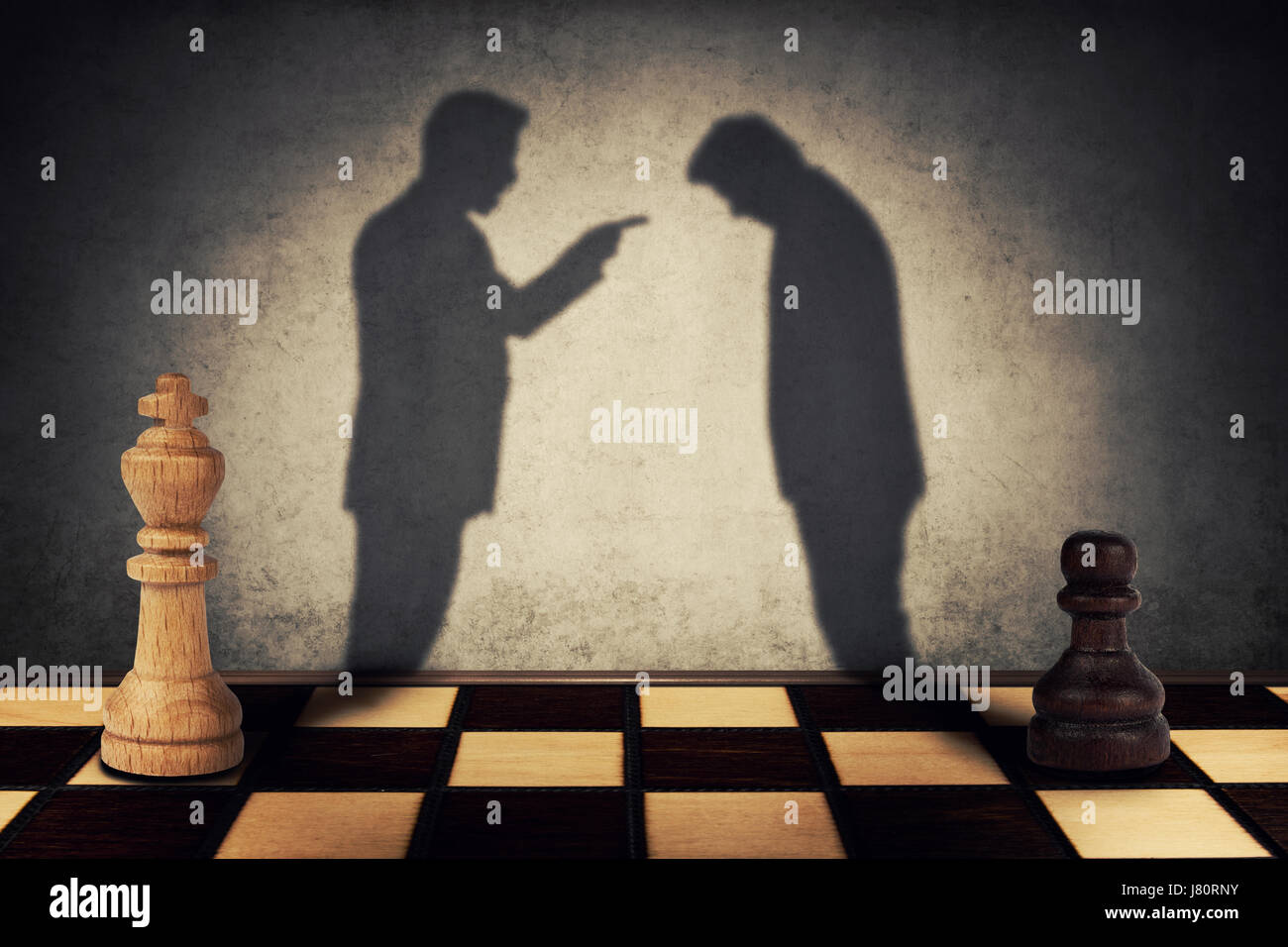 Chess peón y rey de pie en frente uno del otro con su sombra se transforma en empresario siluetas. Jerarquía de la empresa malentendido concepto Foto de stock