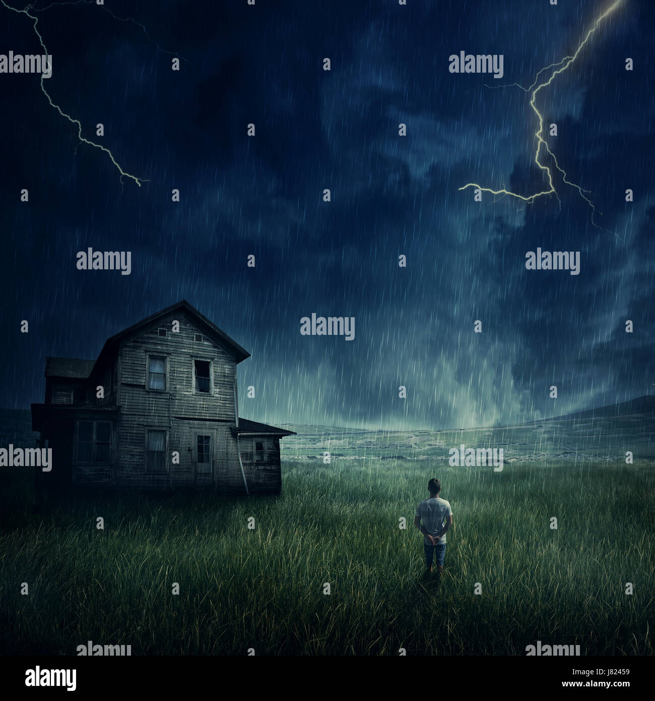 Spooky paisaje como un joven muchacho caminando en la pradera mirar un fantasma, casa embrujada por debajo de un oscuro cielo tormentoso. Foto de stock