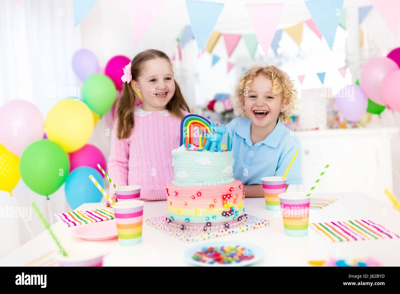 Fiesta de cumpleaños para niños con decoración en tonos pastel y arco iris  de colores pastel. Niña y Niño con dulces, dulces y frutas. Globos y banner  en decora festivo Fotografía de