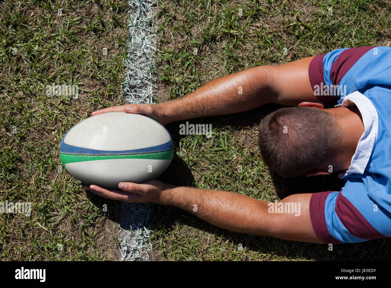 Vista trasera del jugador de rugby sosteniendo la bola en la línea de gol en el campo de juego Foto de stock