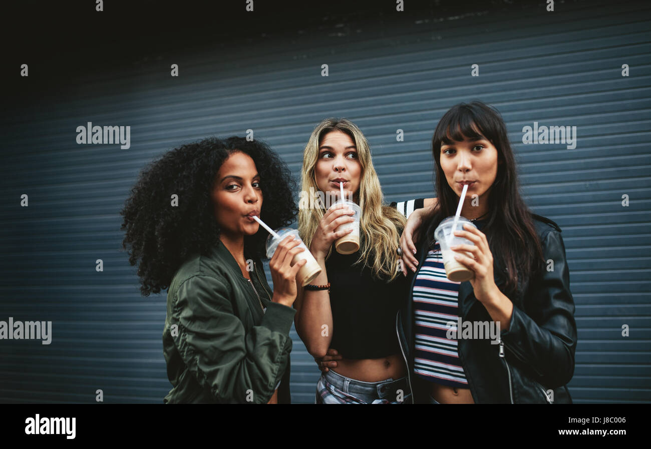 Hermosas hembras jóvenes que ice café al aire libre. Grupo multirracial de mujeres amigas bebiendo café. Foto de stock
