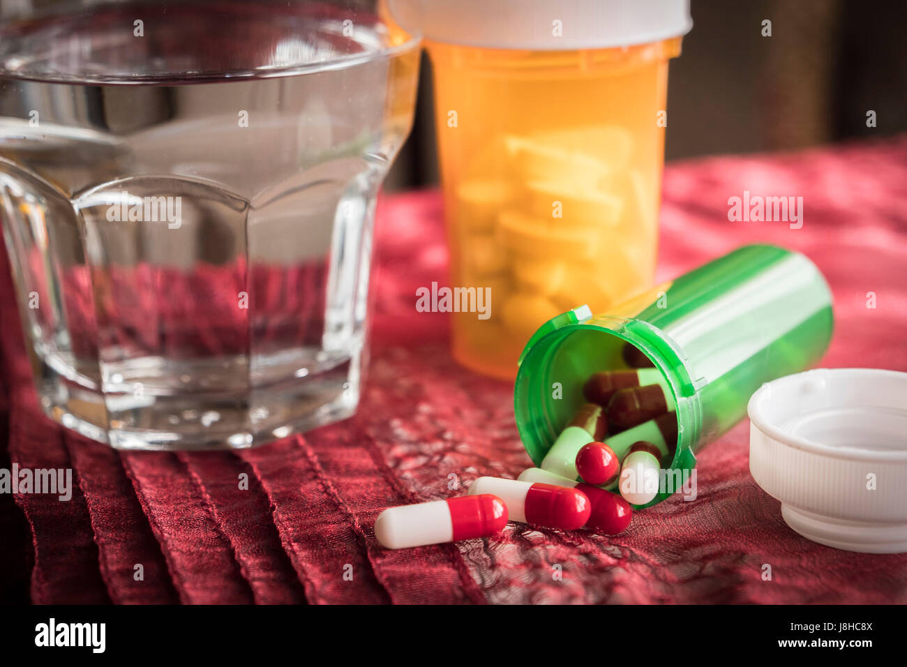 Píldoras blancas y rojas saliendo de una botella verde abierto Foto de stock