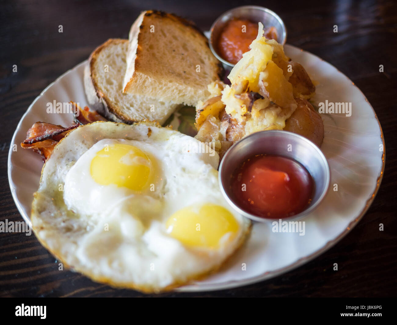 Dos sunny side up huevos, papas ralladas, tostadas, agrio y tocino canadiense (desayuno) de Chartier Restaurante en Beaumont, Alberta, Canadá. Foto de stock