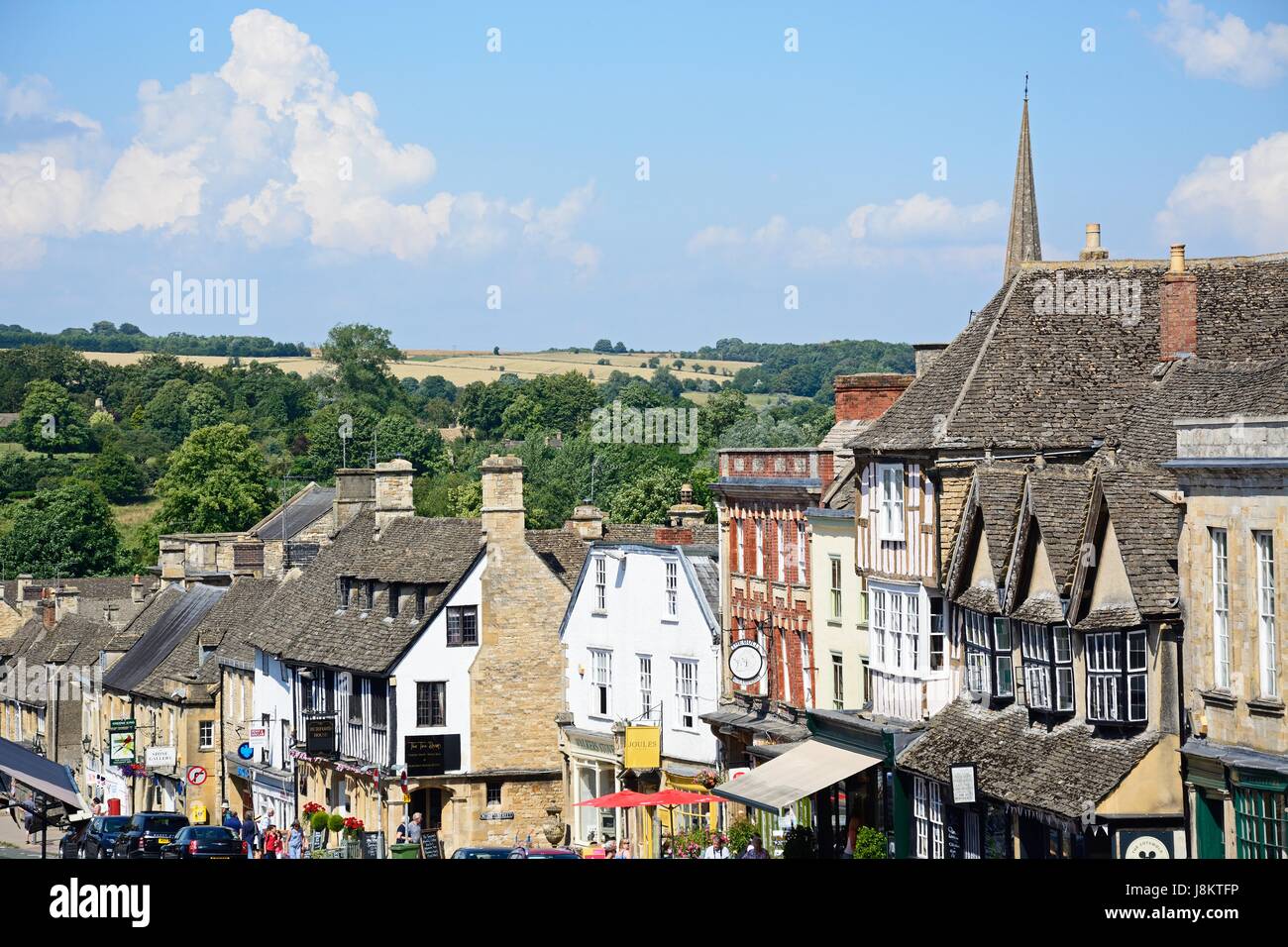 Vista de comercios y empresas a lo largo de la colina calle comercial durante la temporada de verano, el Burford, Oxfordshire, Inglaterra, Reino Unido, Europa Occidental. Foto de stock