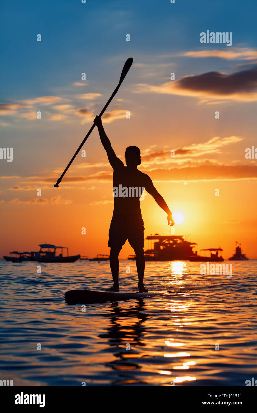 Paddle boarder. Sunset silueta negra del joven deportista remando en stand up paddleboard. Estilo de vida saludable. Deporte acuático, SUP surf tour en adven Foto de stock