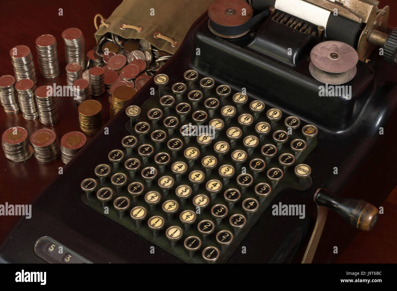 Black Antique calculadora con botones pulsadores mecánicos y algunas monedas pilas junto a ella. Foto de stock