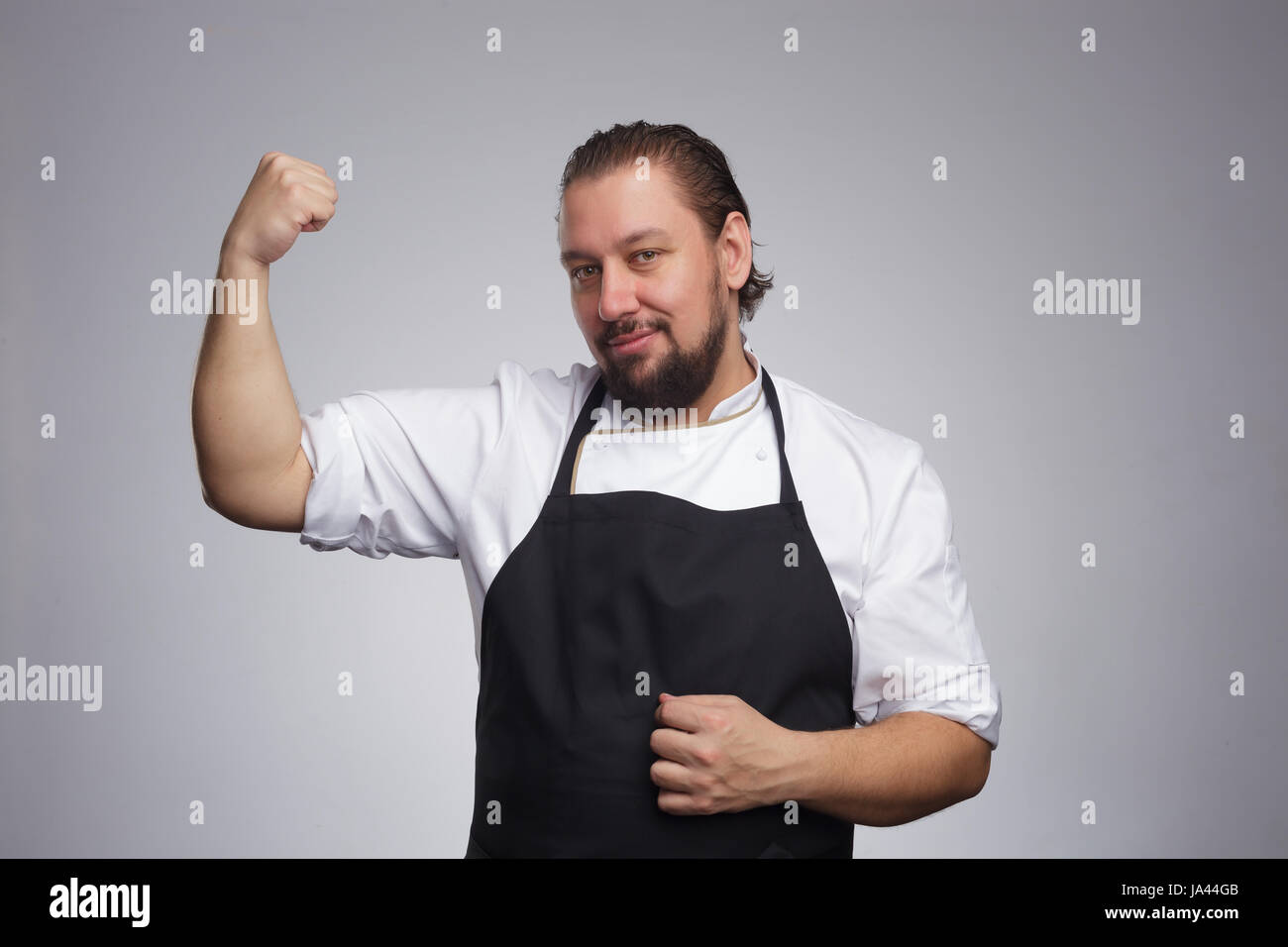 Cocinar en un delantal negro muestra muscular de brazo. Resultados de una nutrición adecuada y un estilo de vida saludable Foto de stock