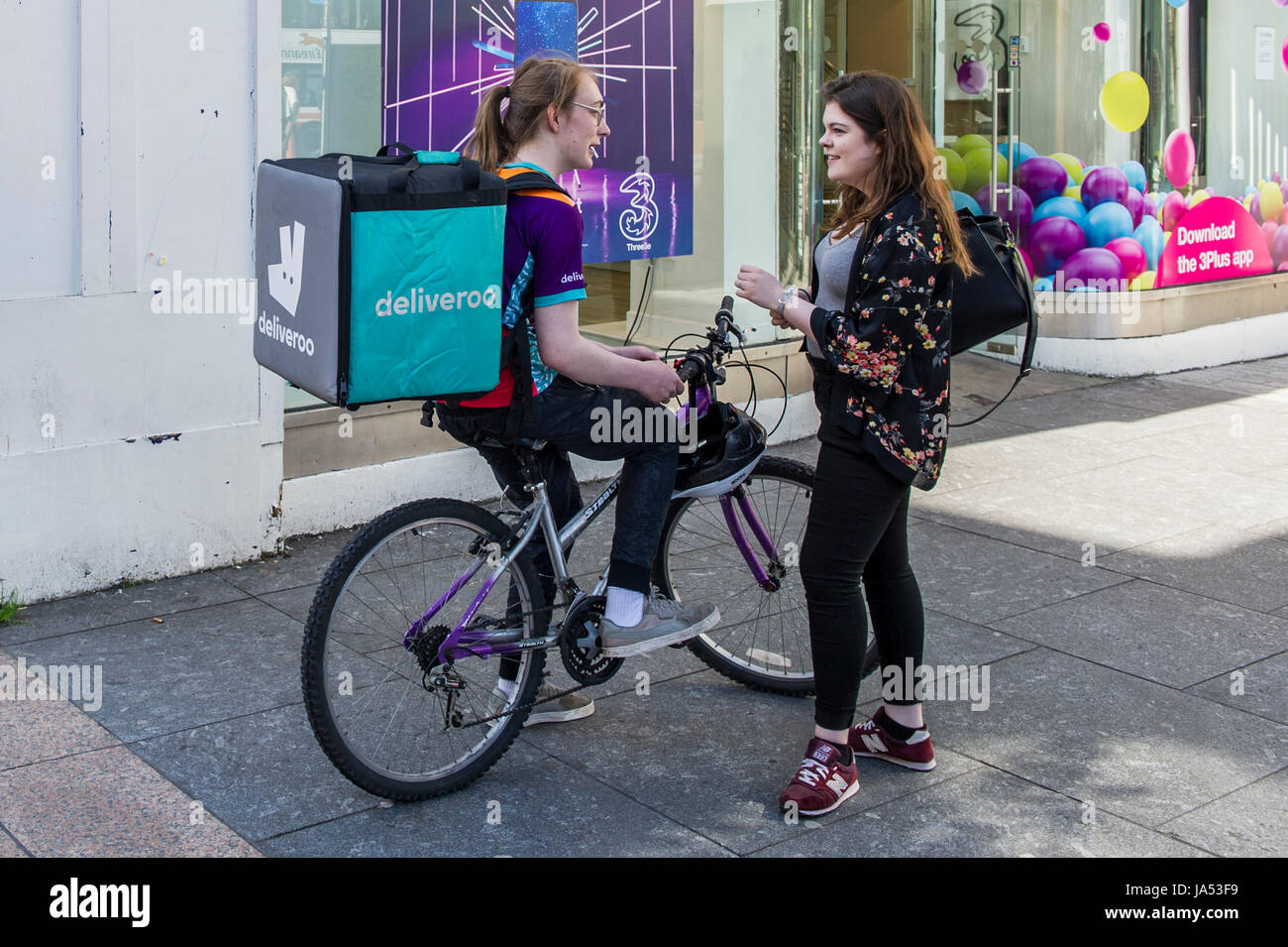 Entrega hembra Deliveroo rider charlando con un amigo durante una estancia en Cork, Irlanda. Foto de stock