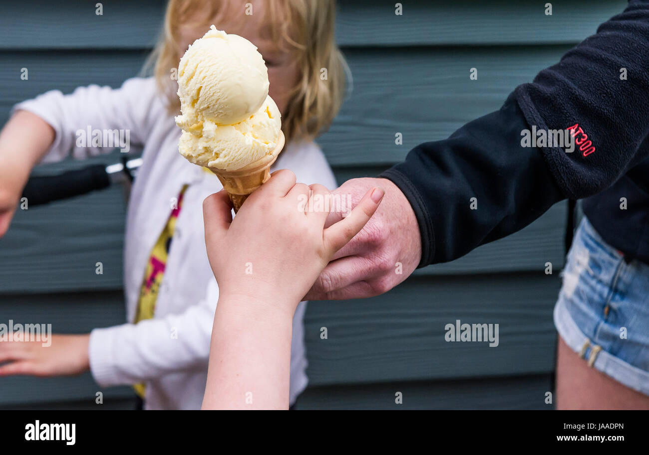Un adulto dando un cucurucho de helado a un niño. Foto de stock