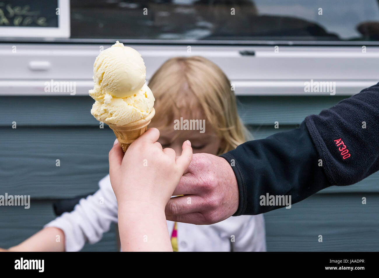 Un adulto dando un cucurucho de helado a un niño. Foto de stock