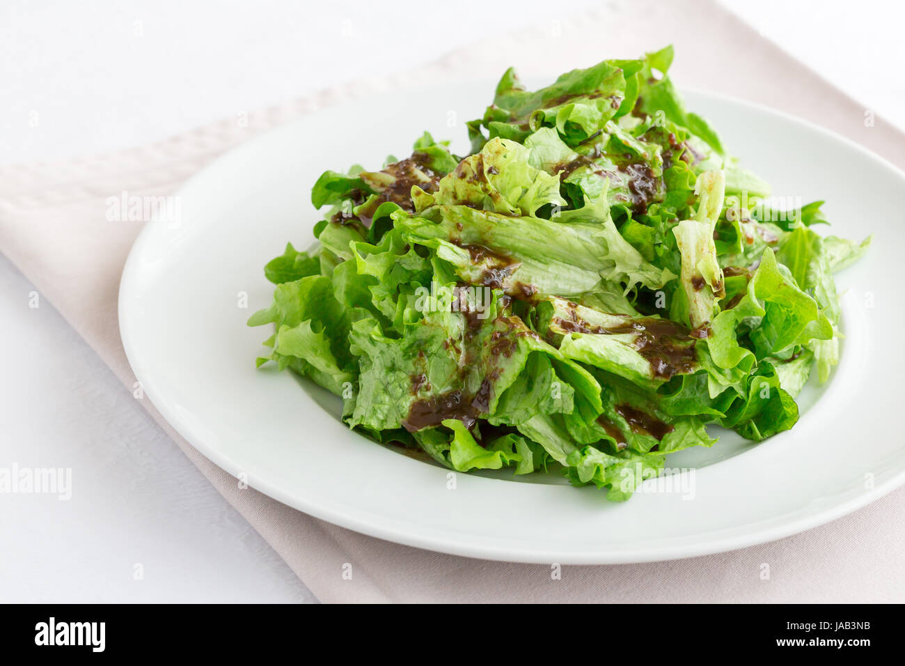 Una ensalada verde mezclada con una salsa de aceite de oliva y vinagre  balsámico en una placa blanca servida en un restaurante. Esta receta es  recomendable para una dieta o d Fotografía