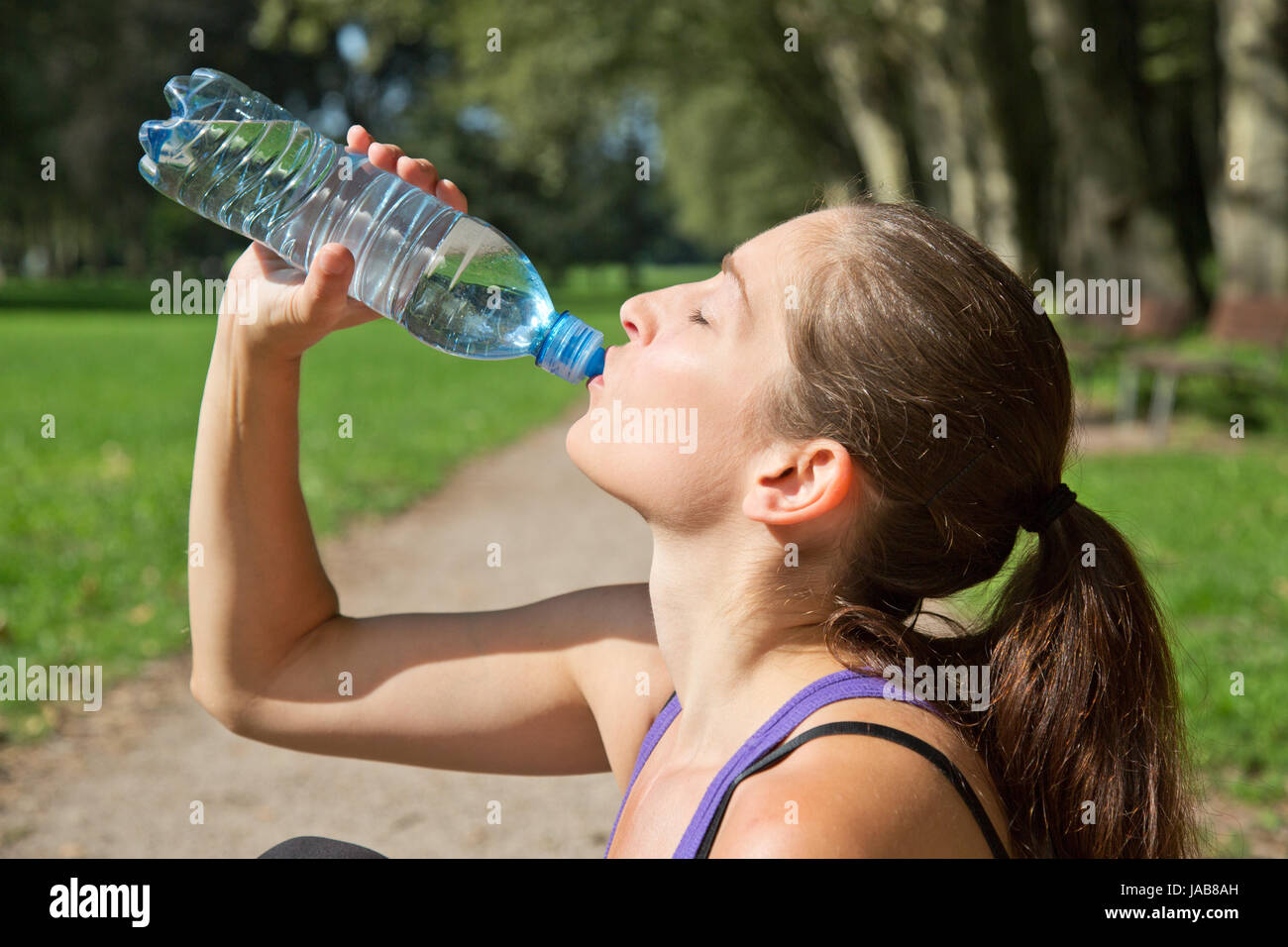 Eine attraktive sportliche Frau trinkt Wasser aus einer Flasche beim deporte oder Joggen Foto de stock