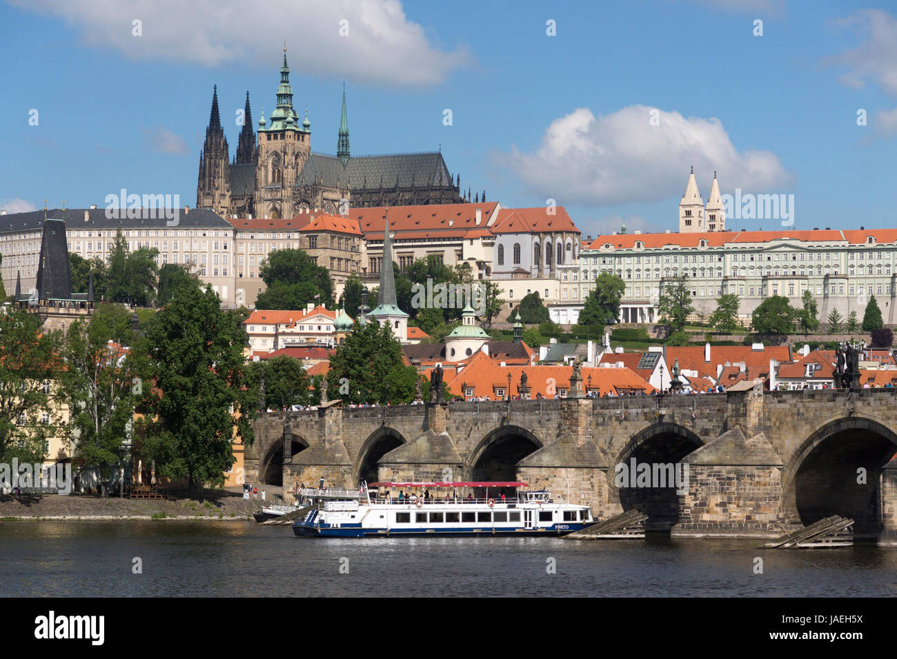Un barco pasa bajo el Puente de Carlos con el castillo de Praga elevándose en el fondo, Praga, República Checa Foto de stock