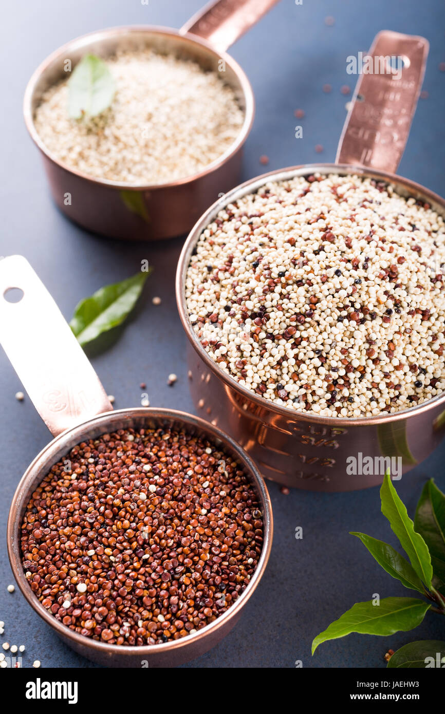 Una pila de tres materias mixtas la quinua, grano de América del Sur, en la bahía de tazas de medir de cobre con hojas de laurel sobre fondo azul. Saludable y libre de gluten foo Foto de stock