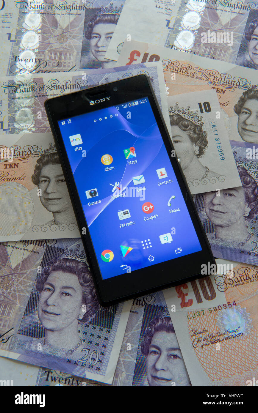 Un teléfono móvil (Android) sobre un fondo de moneda británica Foto de stock