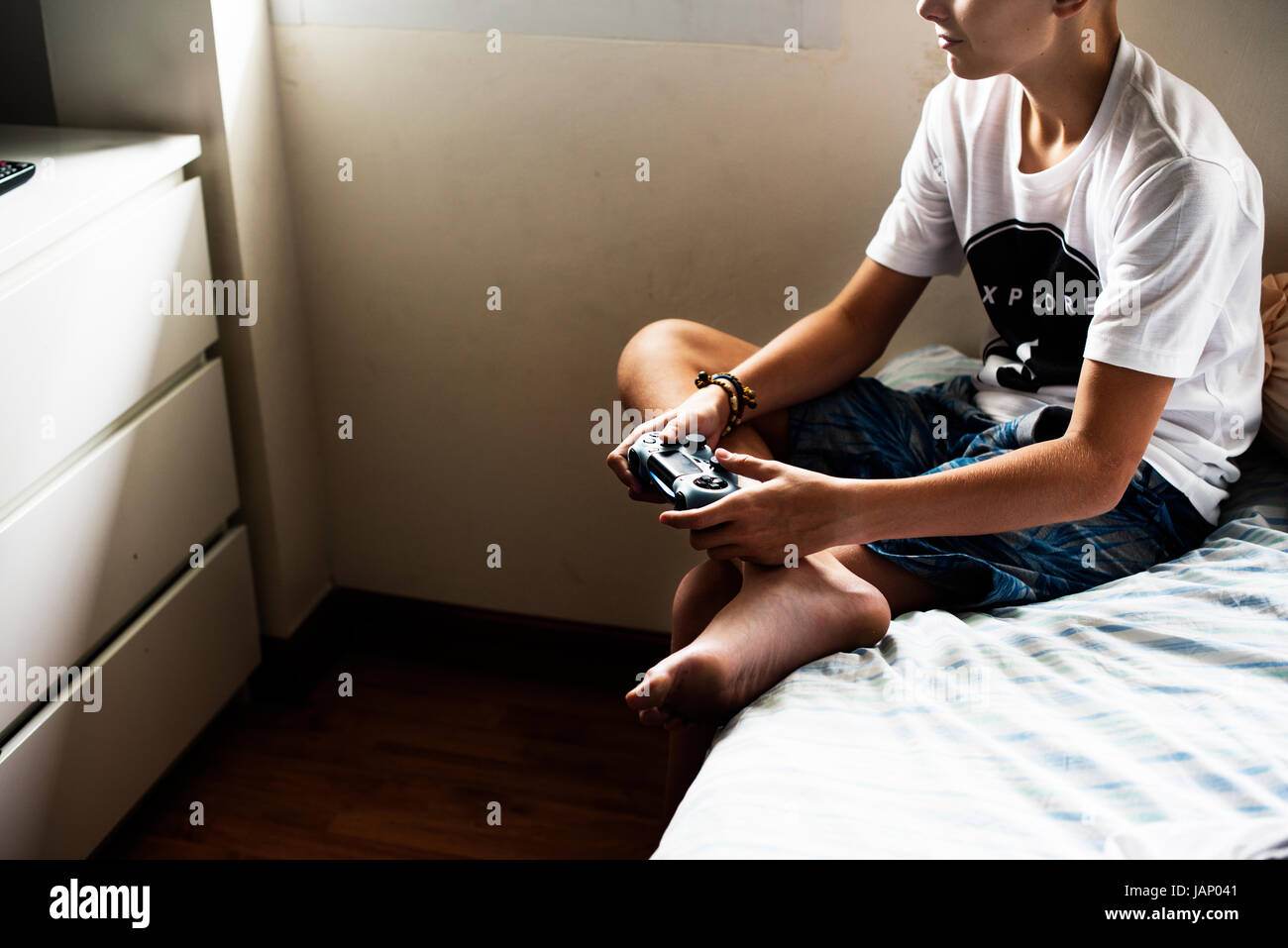 Los jóvenes caucásicos niño sosteniendo control del juego sentada en la cama Foto de stock