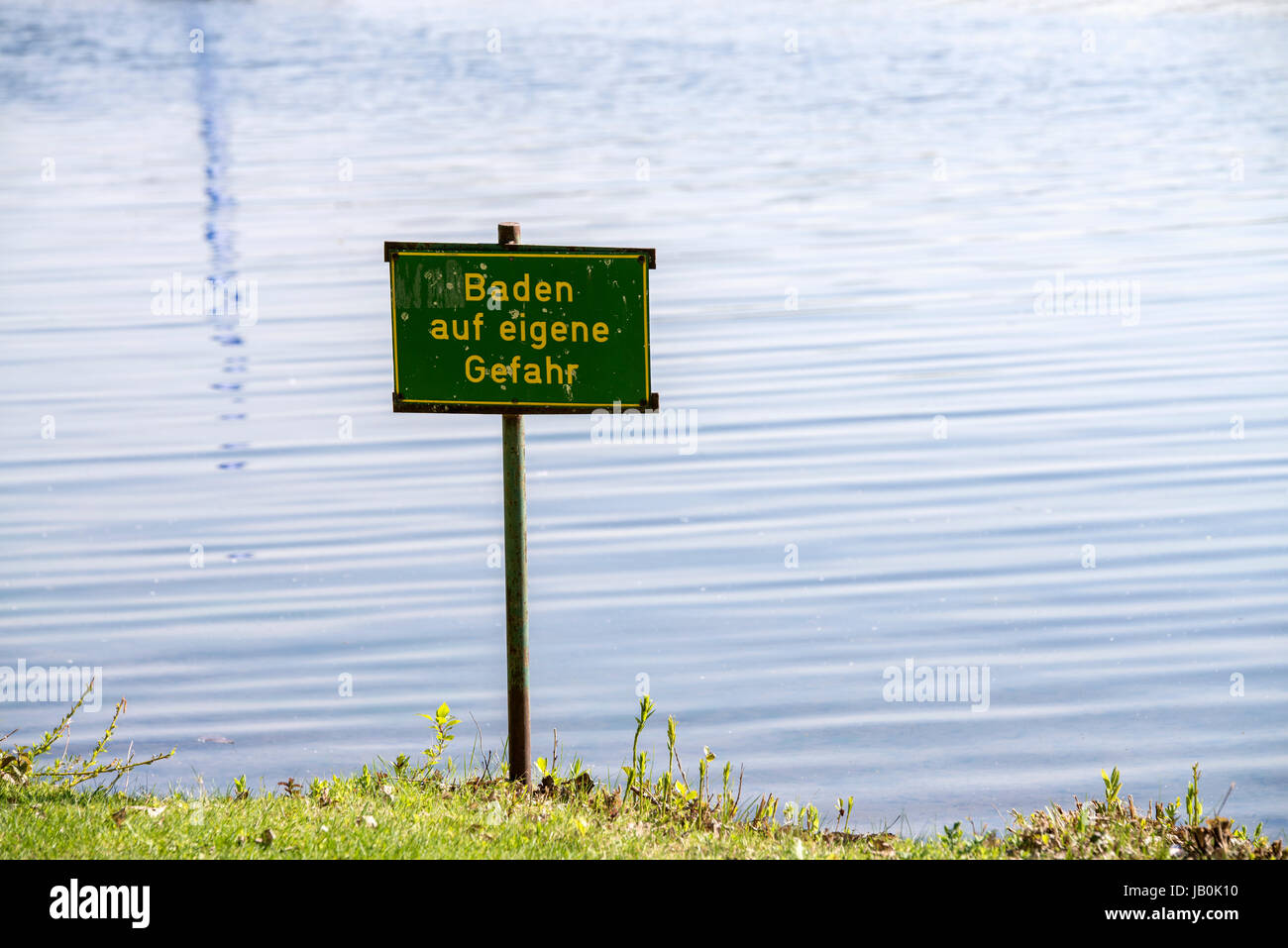 Señal de advertencia con la inscripción "bañarse en su propio riesgo' en un lago. Foto de stock