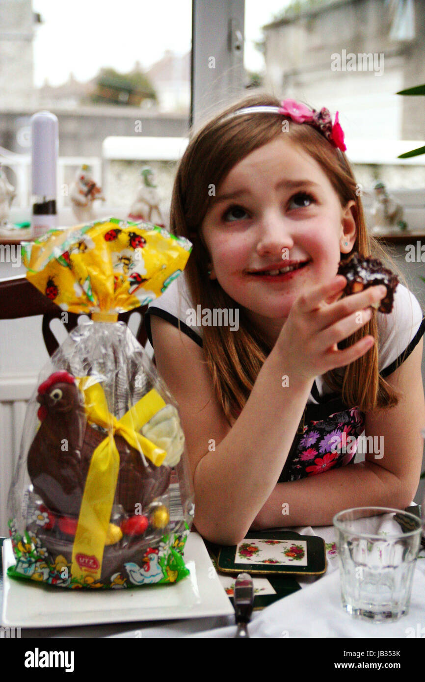 Chica busca encantado de estar comiendo un bizcocho de chocolate el domingo de Pascua con un huevo de pollo chocolate envuelto junto a ella Foto de stock