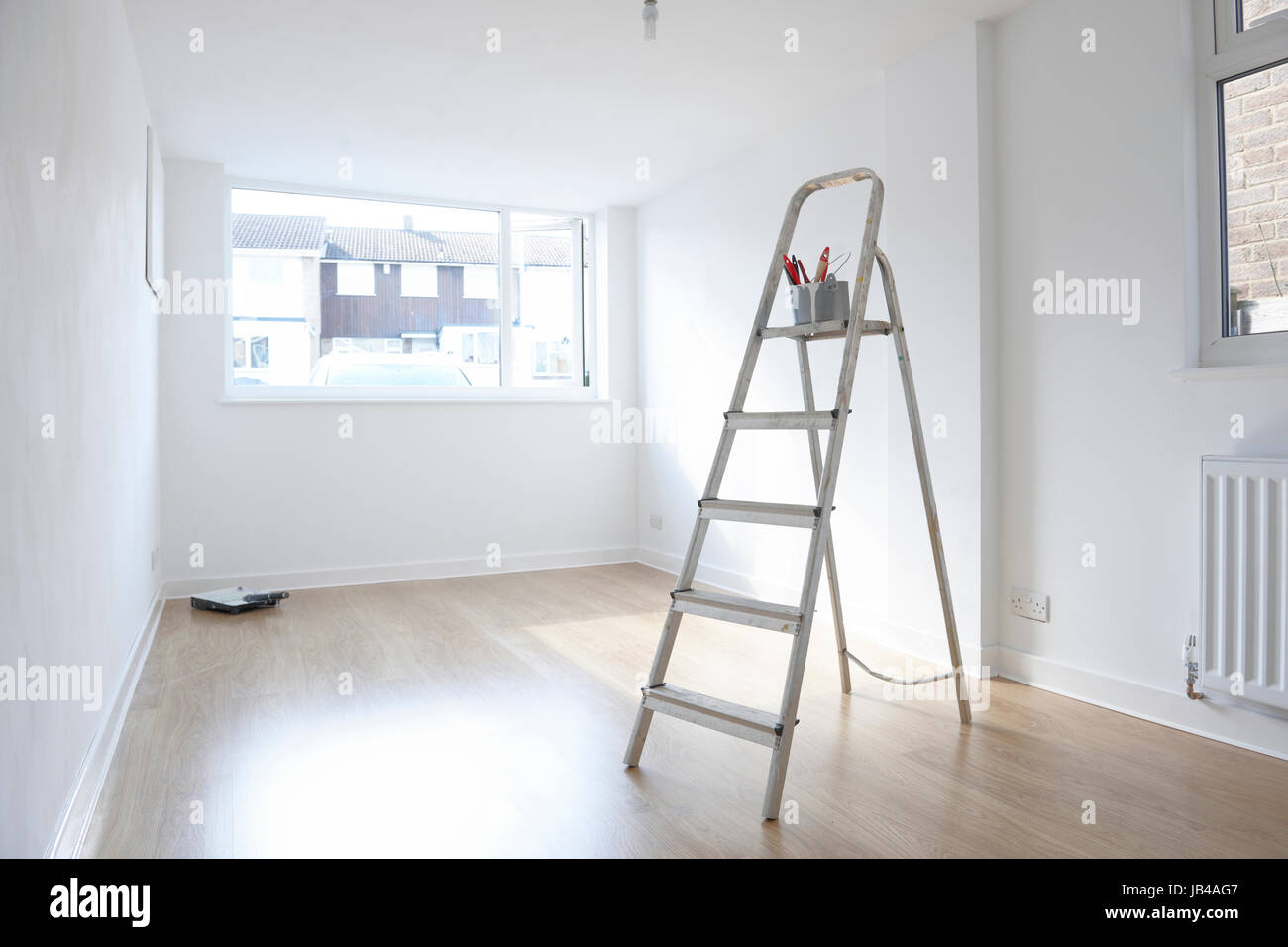 Escalera con Bote de pintura y pinceles de pie en una habitación vacía Foto de stock