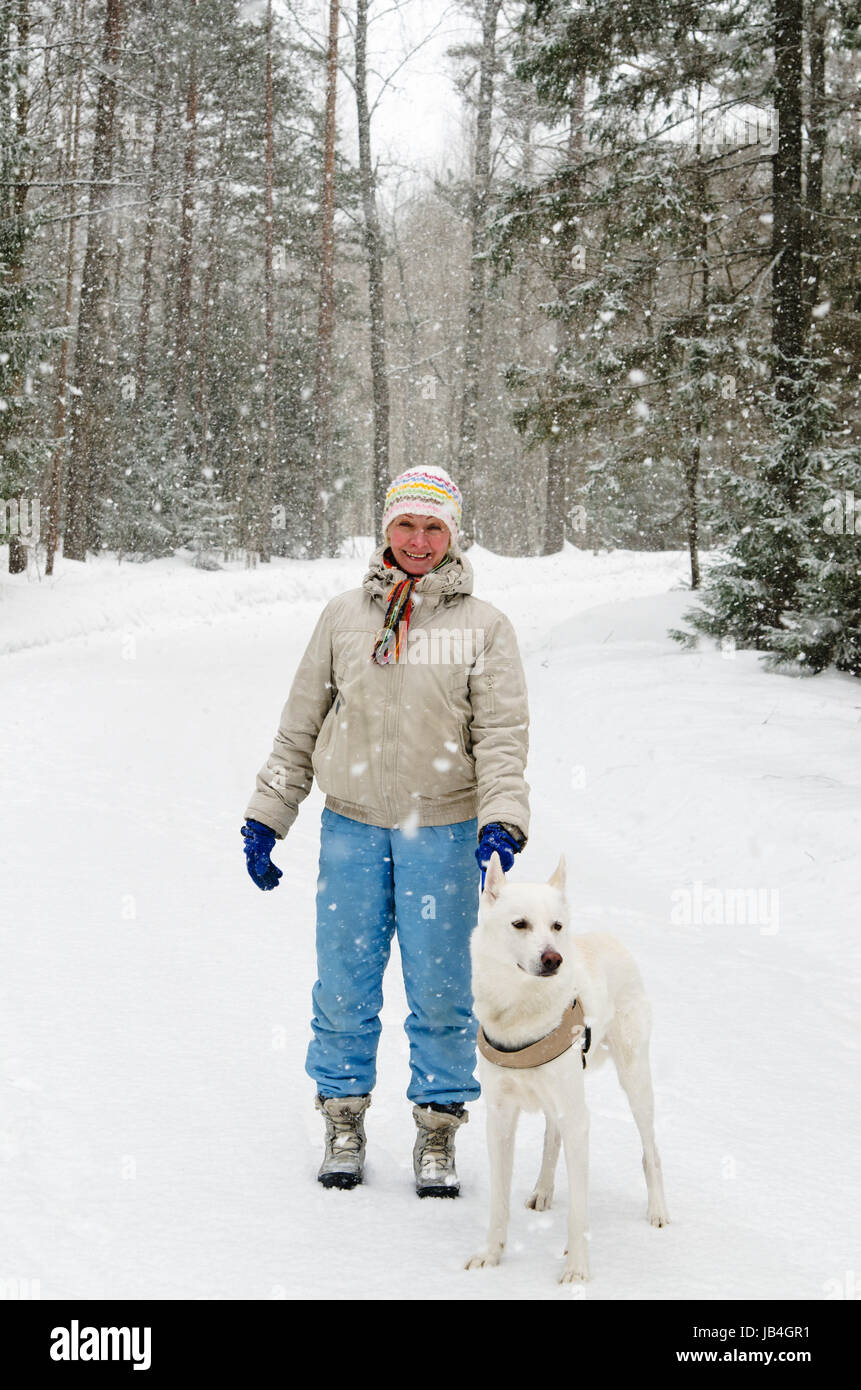 Mujer con un perro en un paseo en el bosque durante una nevada Foto de stock