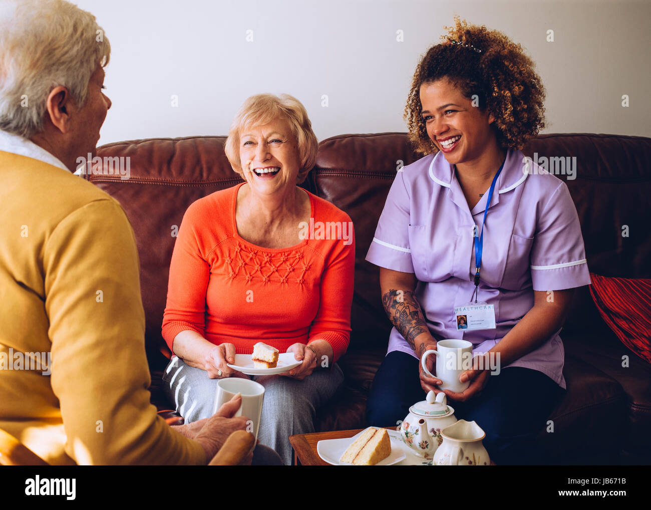 Cuidador ancianos sentados con dos de sus pacientes en el cuidado en casa. Están disfrutando de unos pasteles y té. Foto de stock