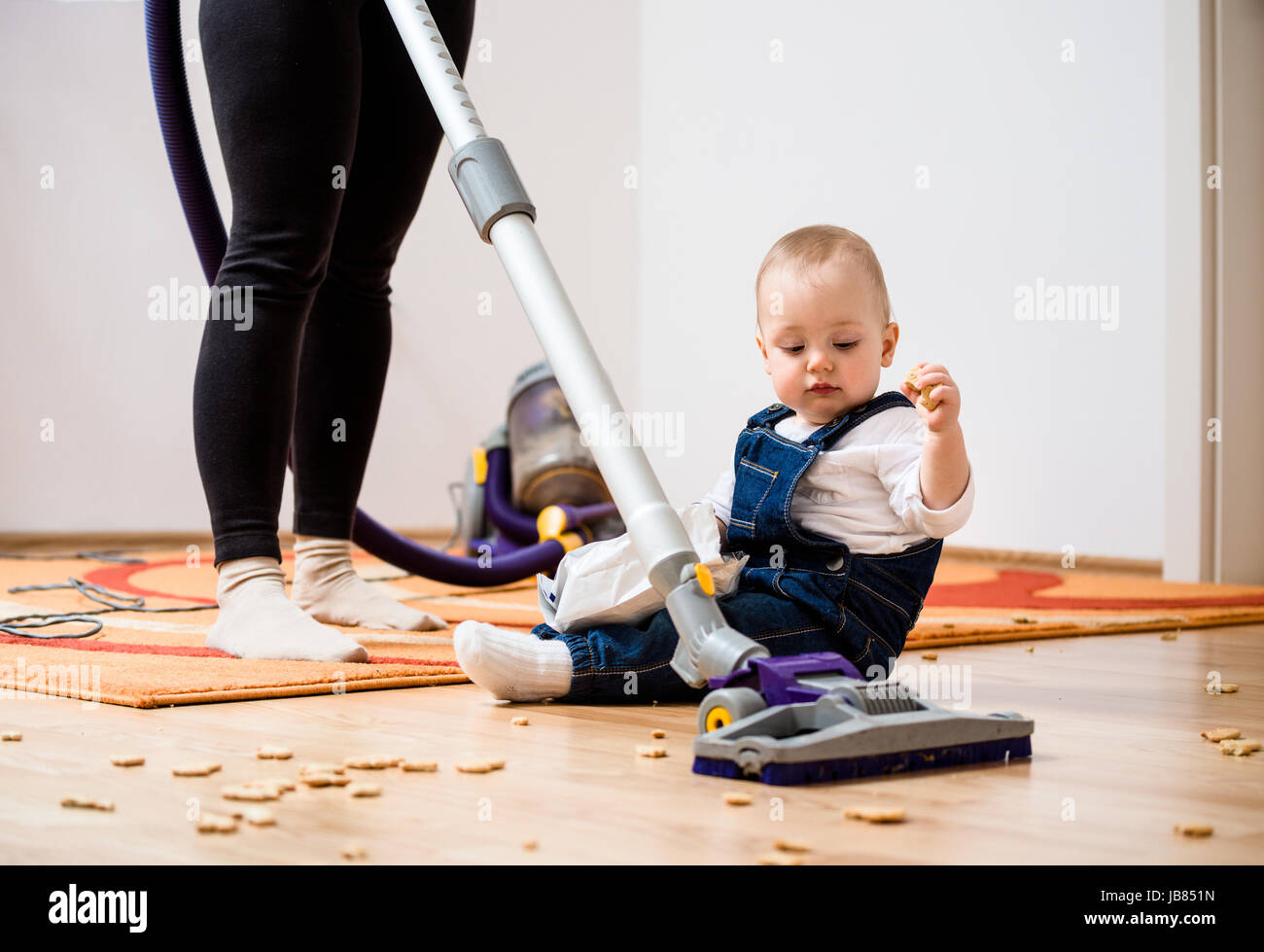 Mujer limpiar con aspiradora, bebé sentado en el piso y galletas todo  Fotografía de stock - Alamy